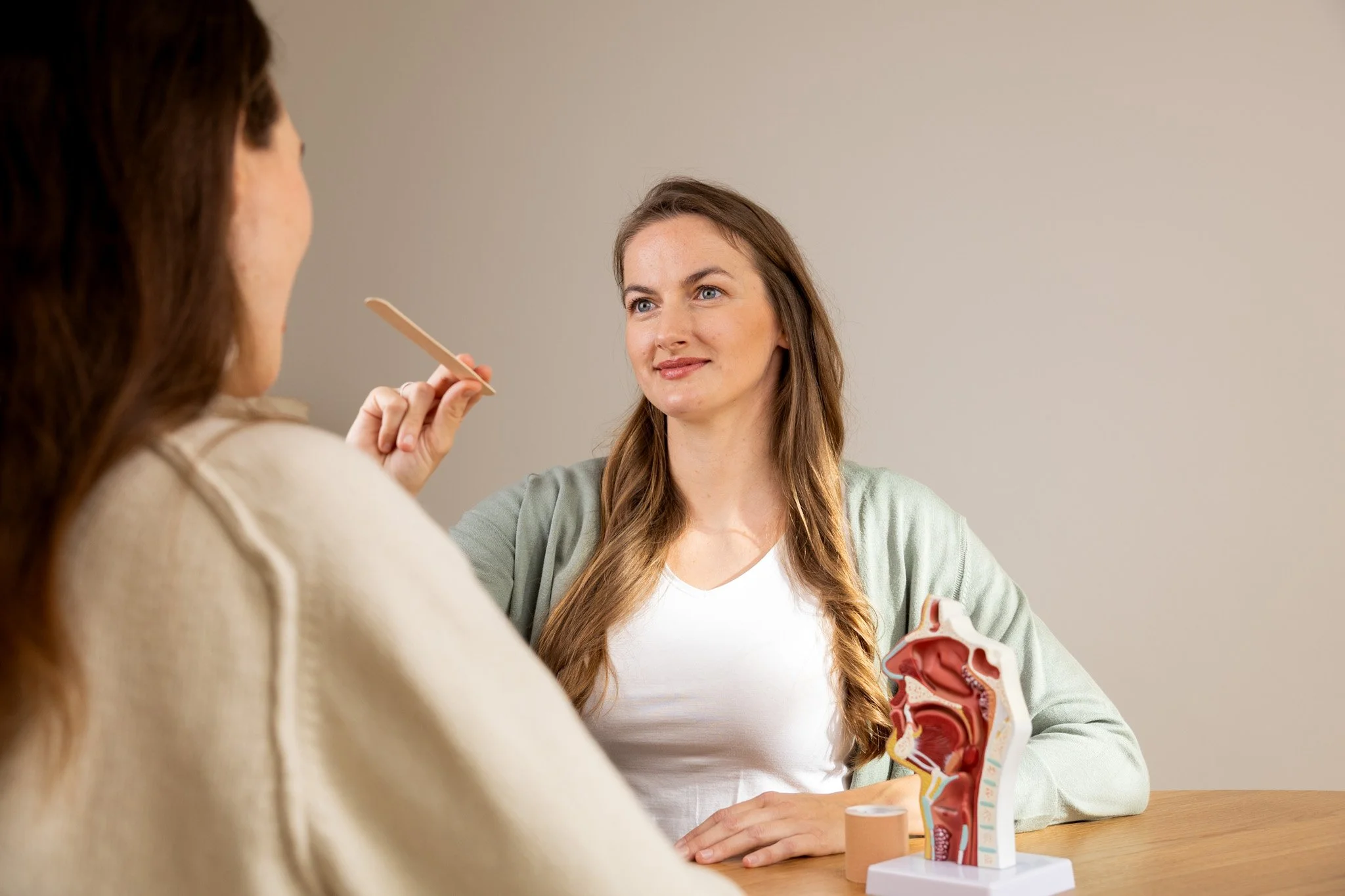 Ärztin erklärt einer Patientin die Anatomie des Rachens anhand eines Modells im Behandlungsraum.