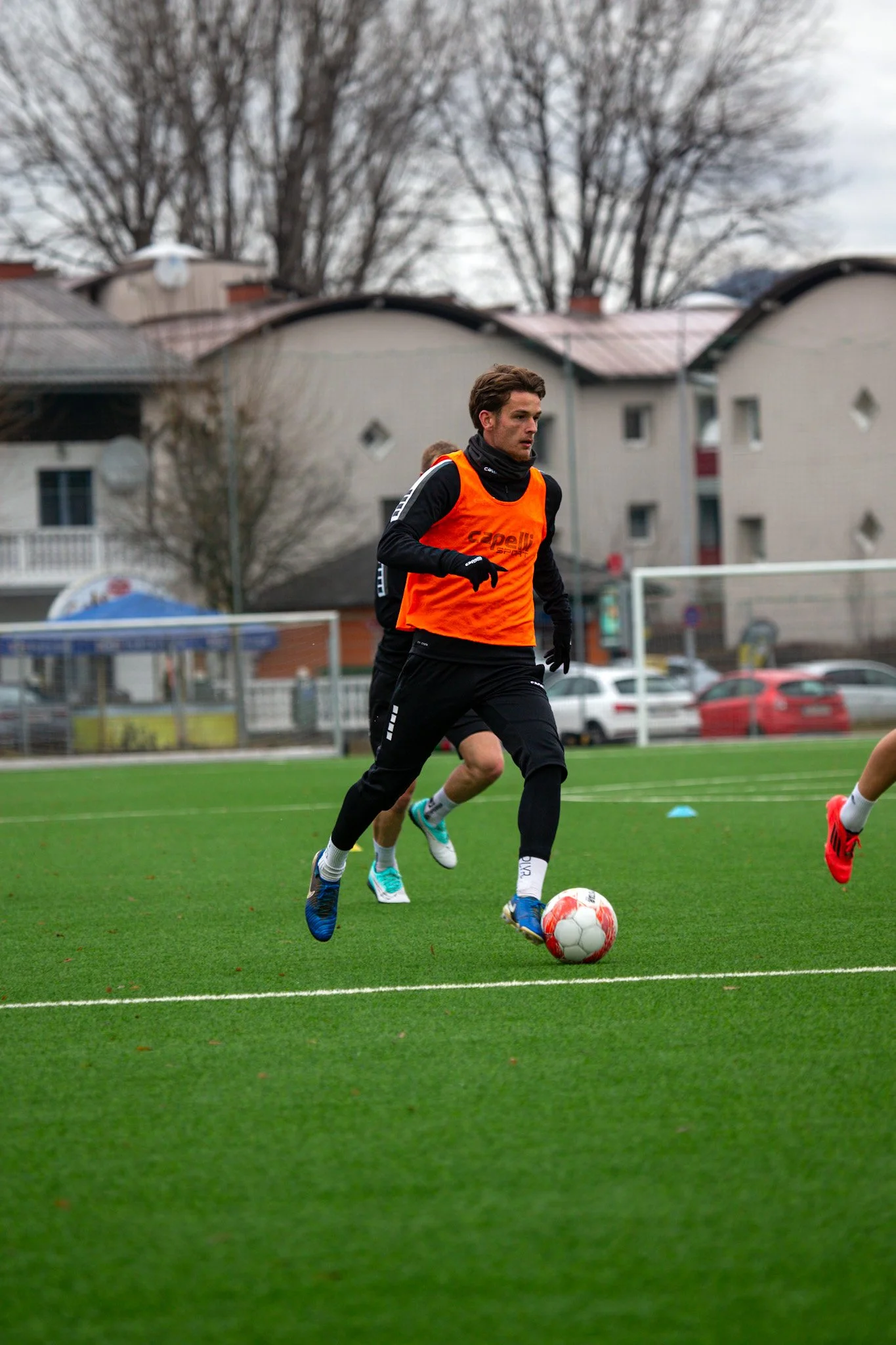Fußballspieler in orangeweste spielt auf einem grünen Fußballfeld.