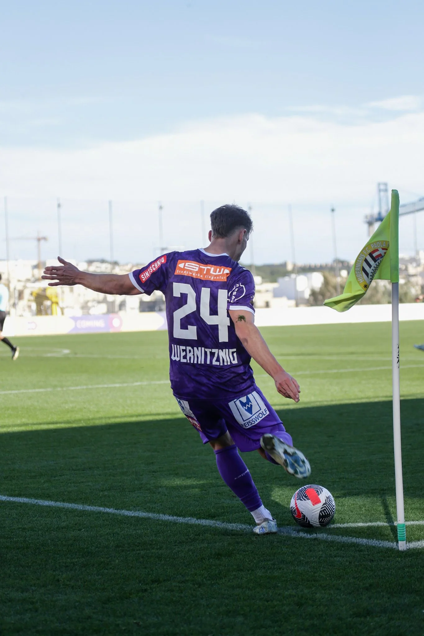 Fußballspieler in purple Trikot beim Schuss am Spielfeldrand, neben Eckfahne auf Rasen.