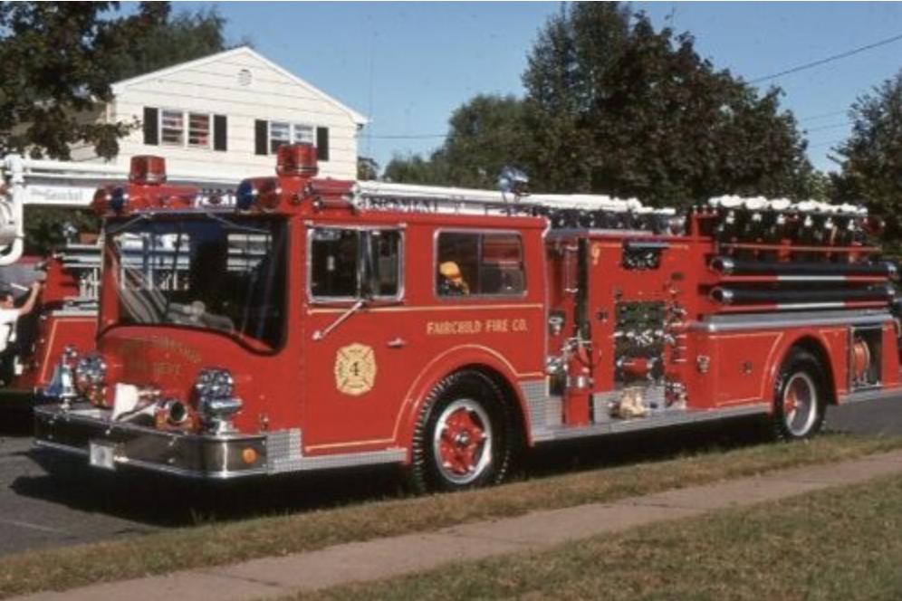 A red fire truck with emergency lights, belonging to the Fairfield Fire Company, parked on a street with a house and trees in the background.