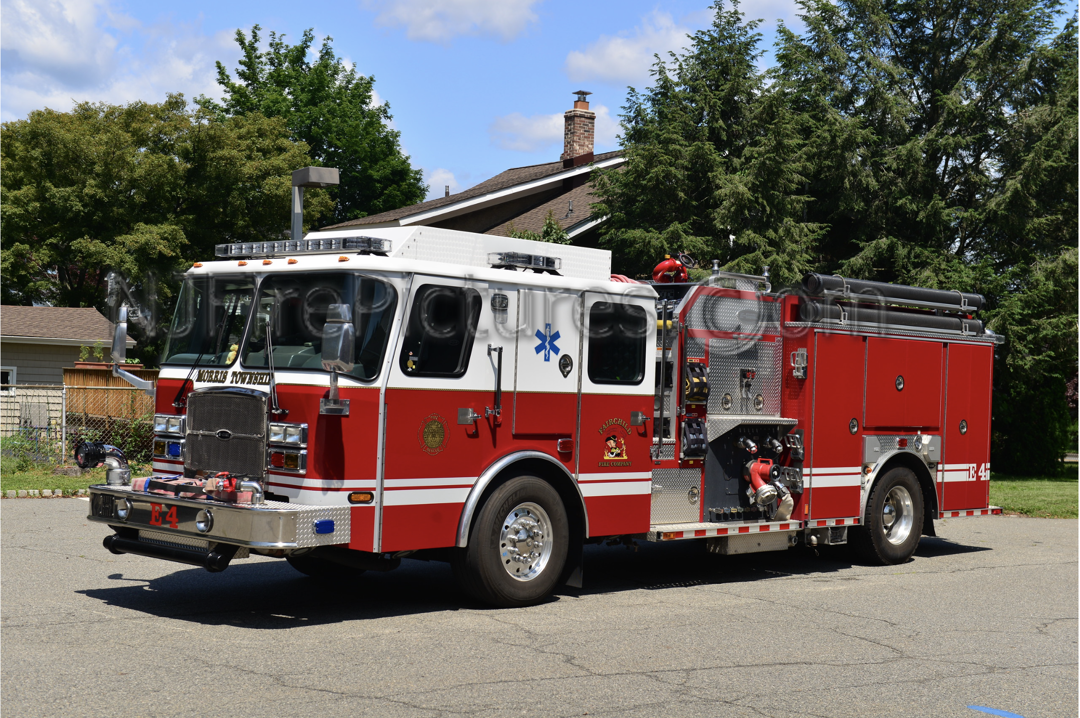 Red and white fire truck parked outdoors on pavement with trees and houses in the background.