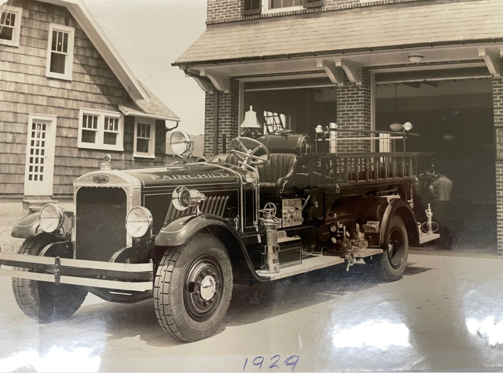 An old-fashioned fire truck parked in front of brick buildings, with the year 1929 written below.
