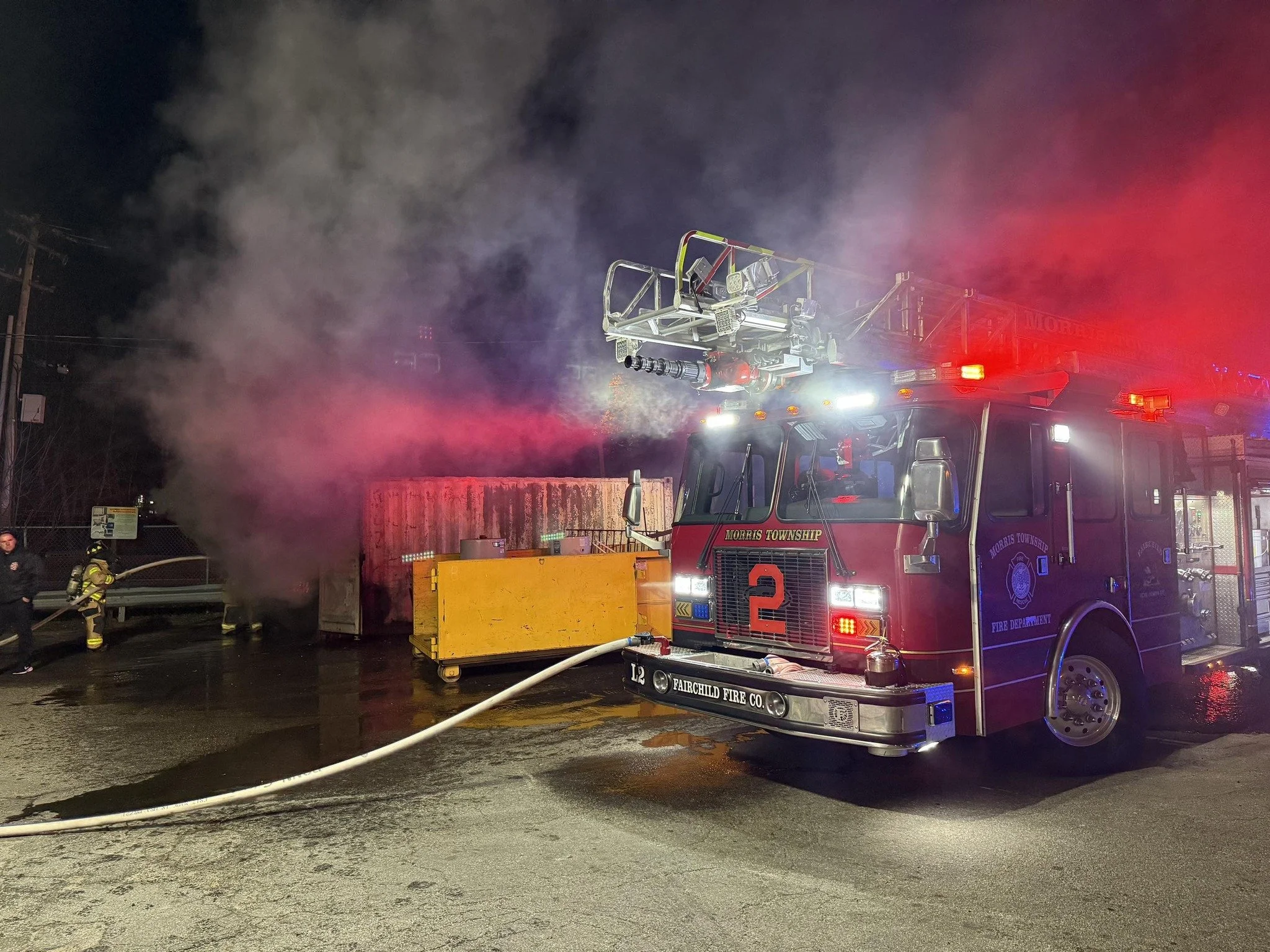 Fire truck from Morris Township Fire Department responding to a fire, with firefighters spraying water on smoke coming from a structure at night.