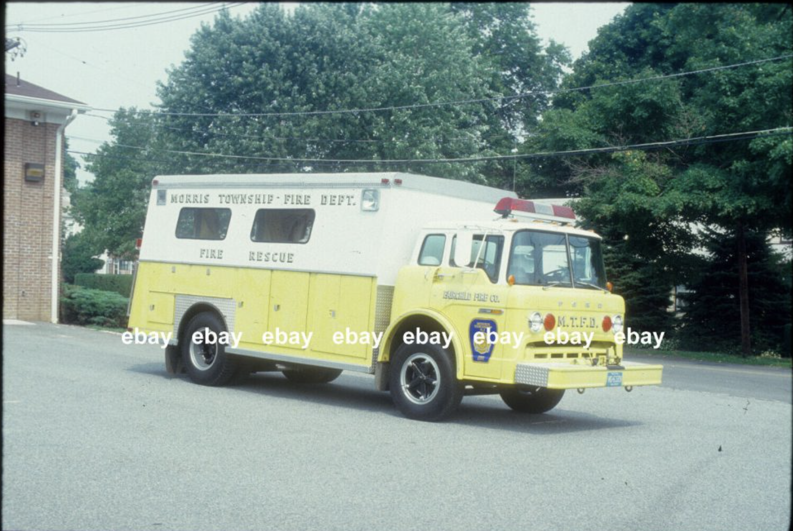 Yellow fire rescue truck parked on street, marked with 'Morris Township Fire Dept.', 'Fire Rescue,' and 'F.O.I.R.C. 12334' on the front, with green trees and a brick building in the background.