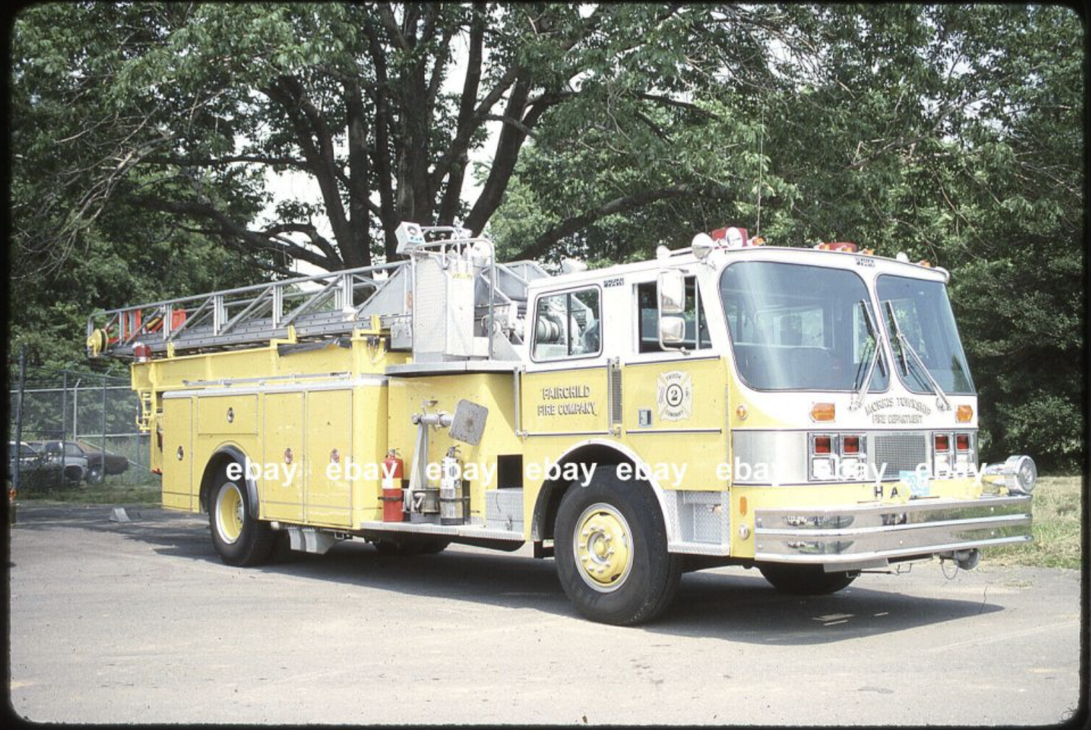 Yellow fire truck with ladder on top, parked outdoors with trees in the background.
