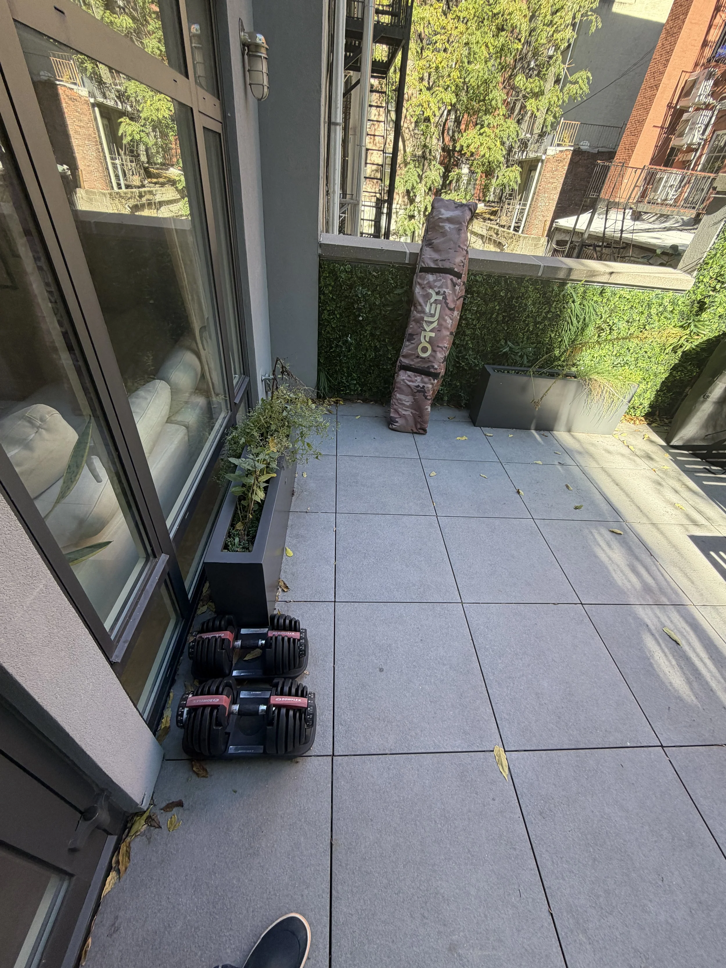Gray terrace paving with scattered leaves beside planters and floor-to-ceiling windows.