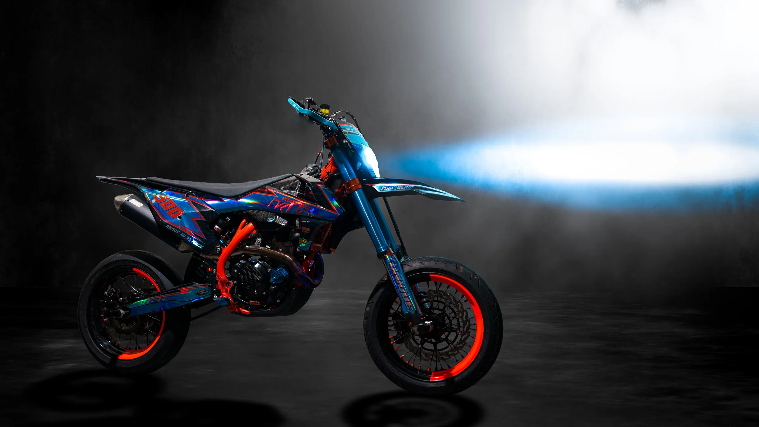 Modernes, bunt gestaltetes KTM Enduro-Motorrad mit leuchtenden orange und blauen Details, auf einem dunklen Hintergrund mit Lichtstrahl, seitliche Ansicht.