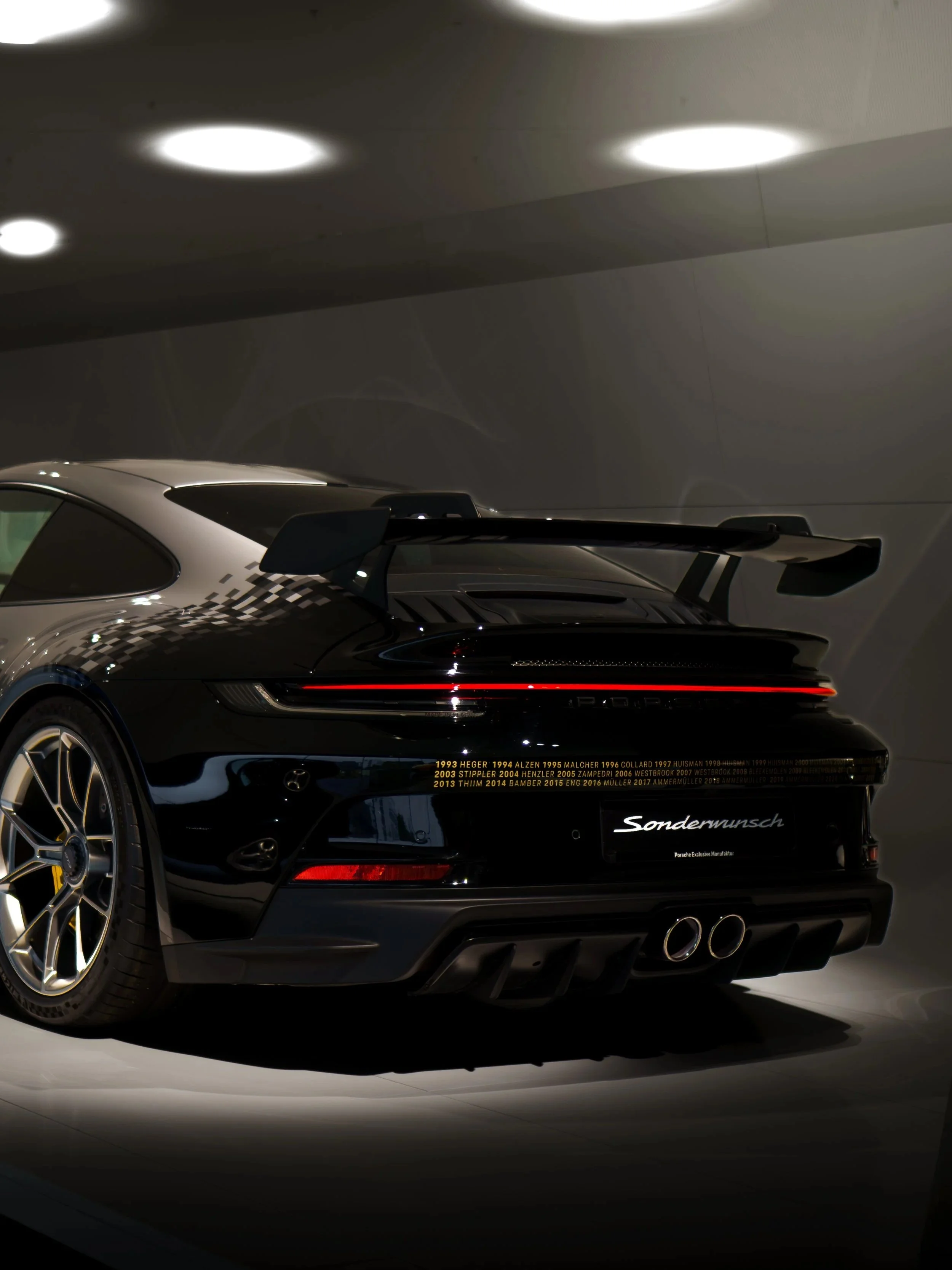 Ein schwarzer Porsche-Sportwagen mit einem großen Heckflügel, stilvoll beleuchtet in einem dunklen Raum.