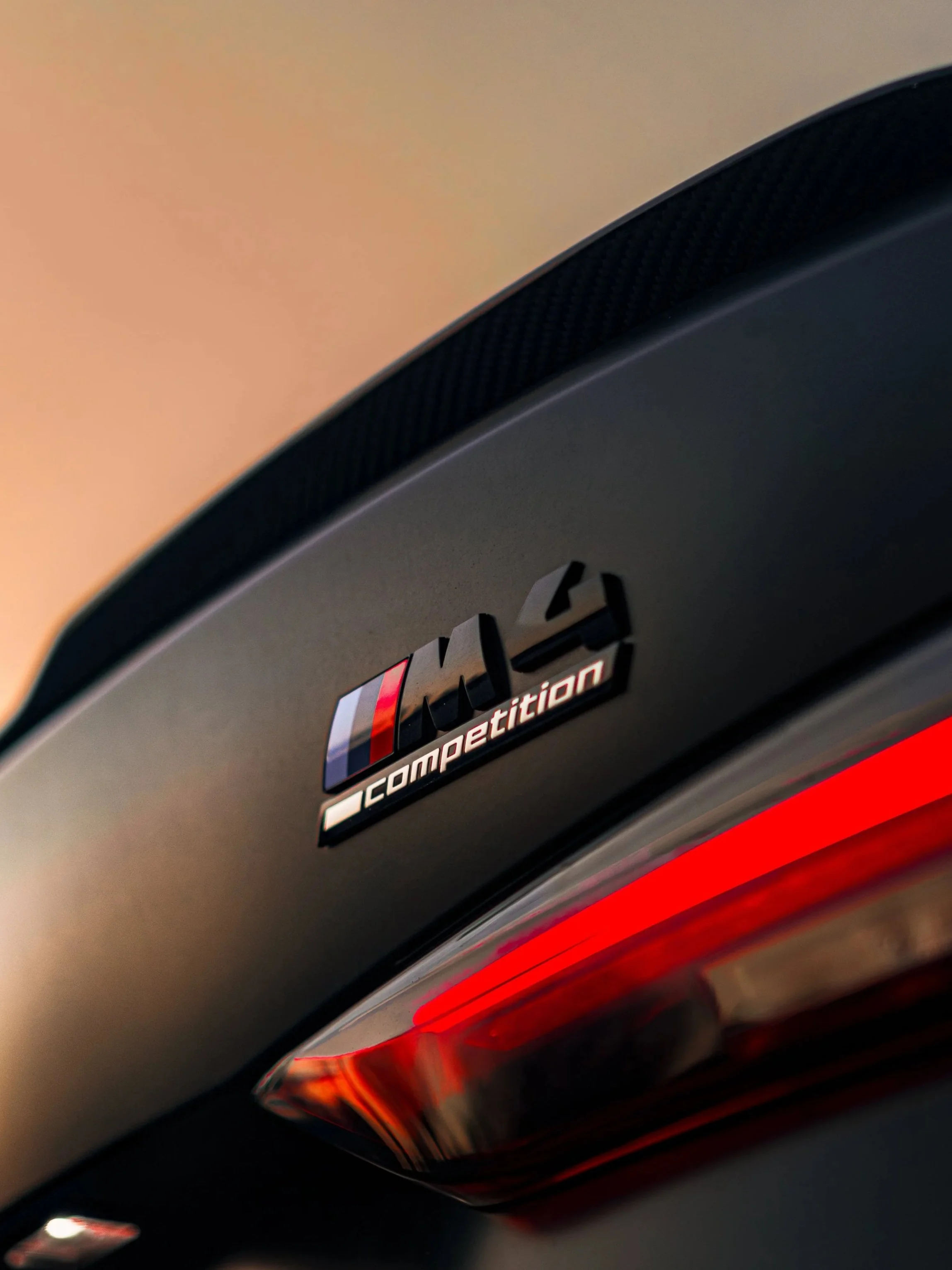 Nahaufnahme des Heckbereichs eines BMW M4 Competition mit Leuchtstoffrückleuchte und M4 Competition-Emblem.