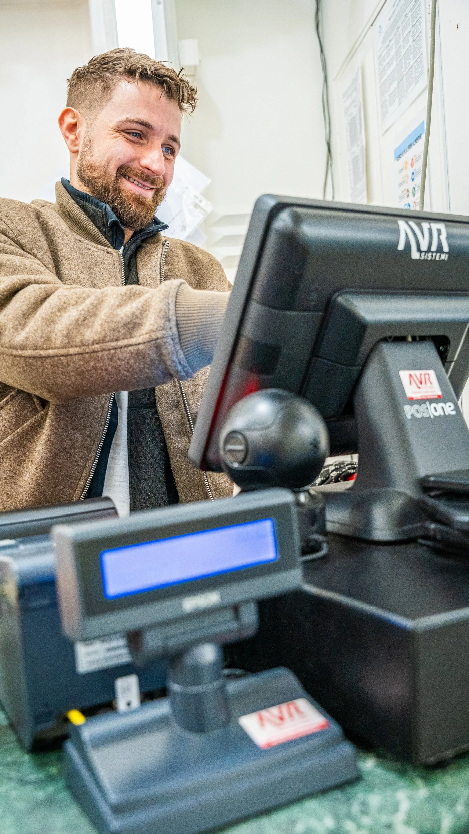 Uomo sorridente che lavora a una cassa con una stampante fiscale sul bancone.