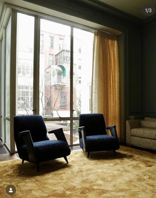 Modern NYC living room with dark green walls, golden yellow drapery and navy blue armchairs