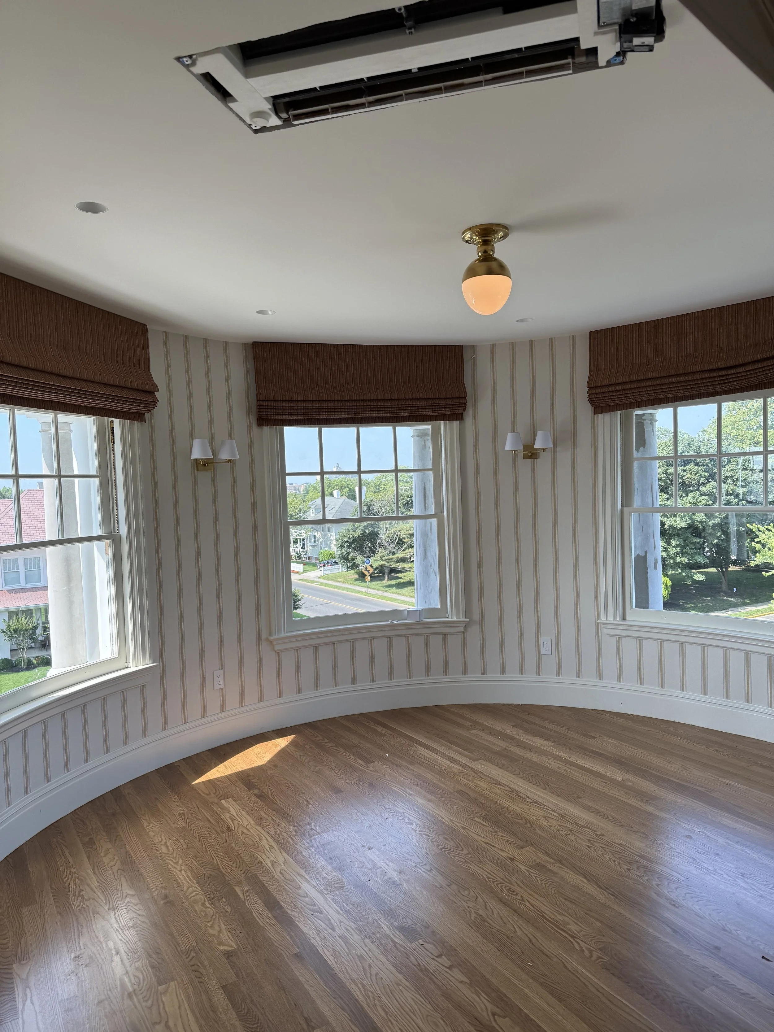 Curved bay window with warm wood roman shades and brass flush mount ceiling light, NYC custom shades