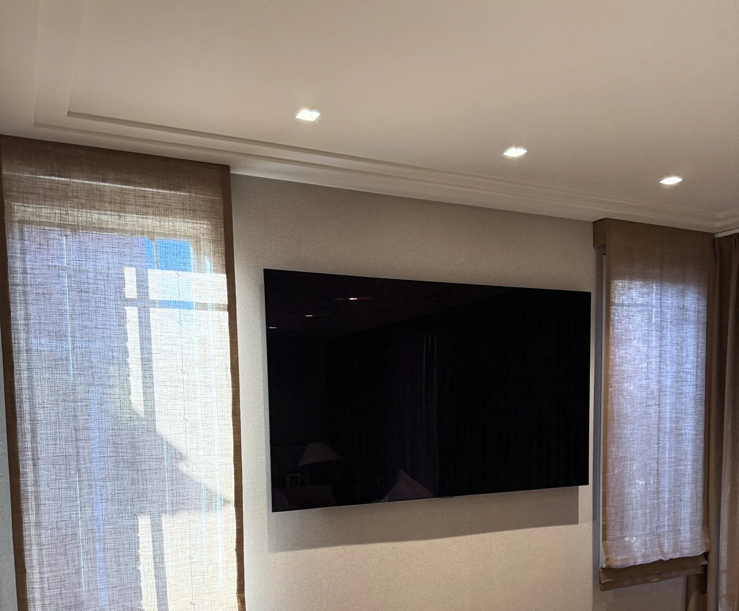 Bordered linen Roman shades flanking a wall-mounted TV in a New York bedroom