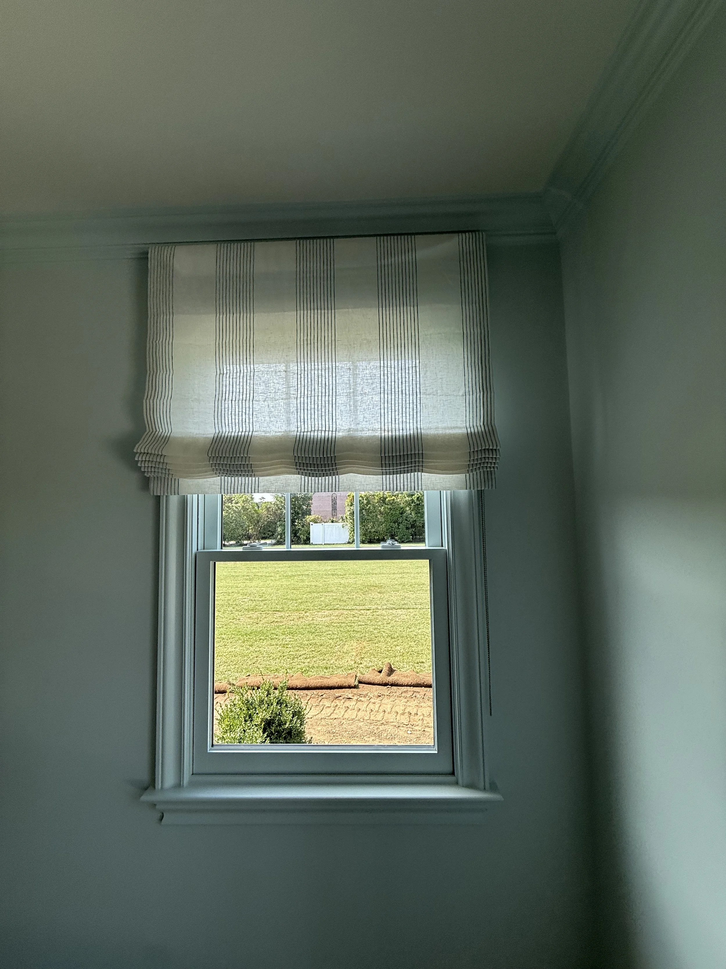 Sheer striped roman shade in sage green painted room with garden meadow view, custom NYC window treatment