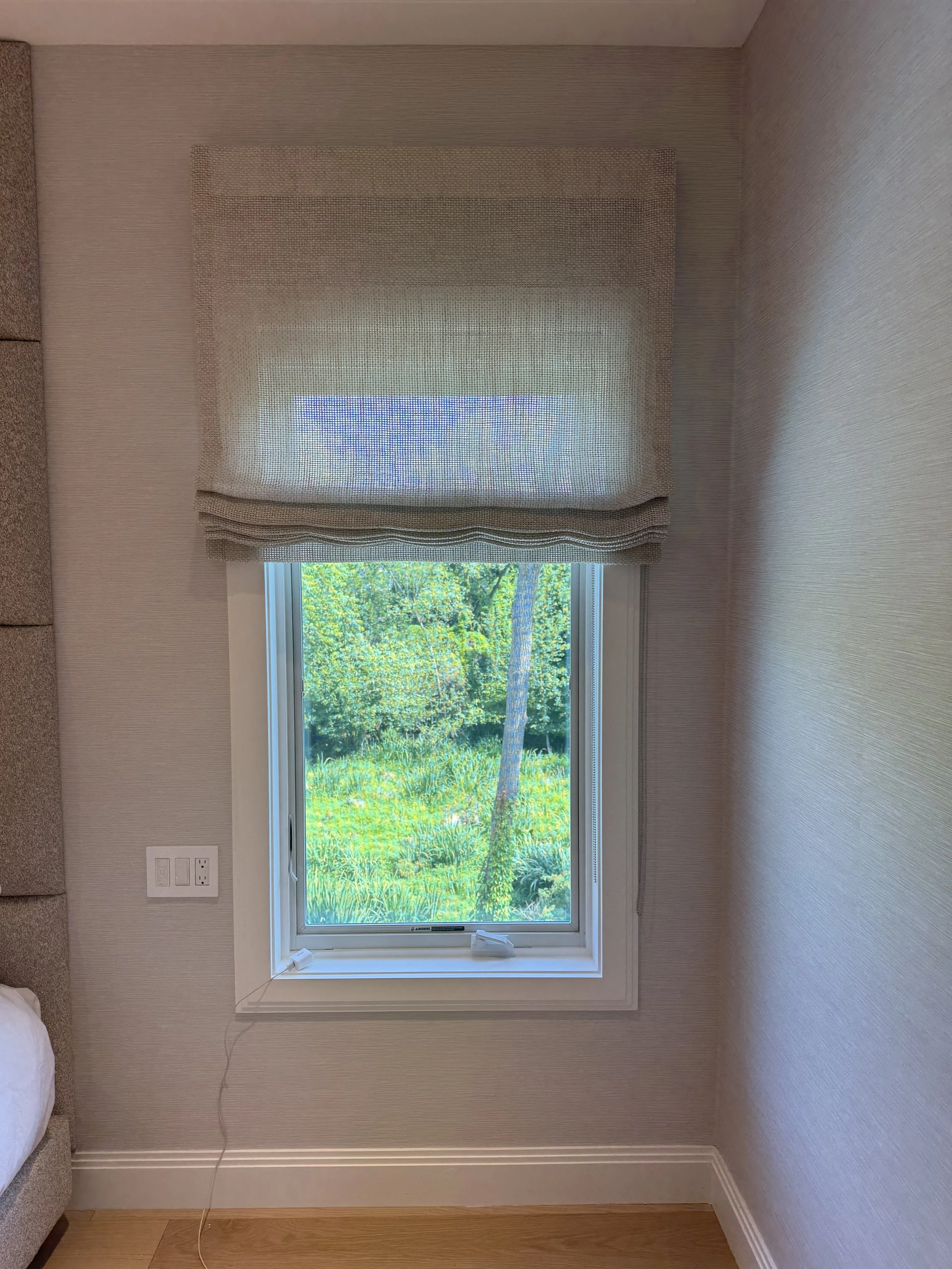 Natural woven roman shade in neutral bedroom with garden views, custom shades NYC Rafael Interiors