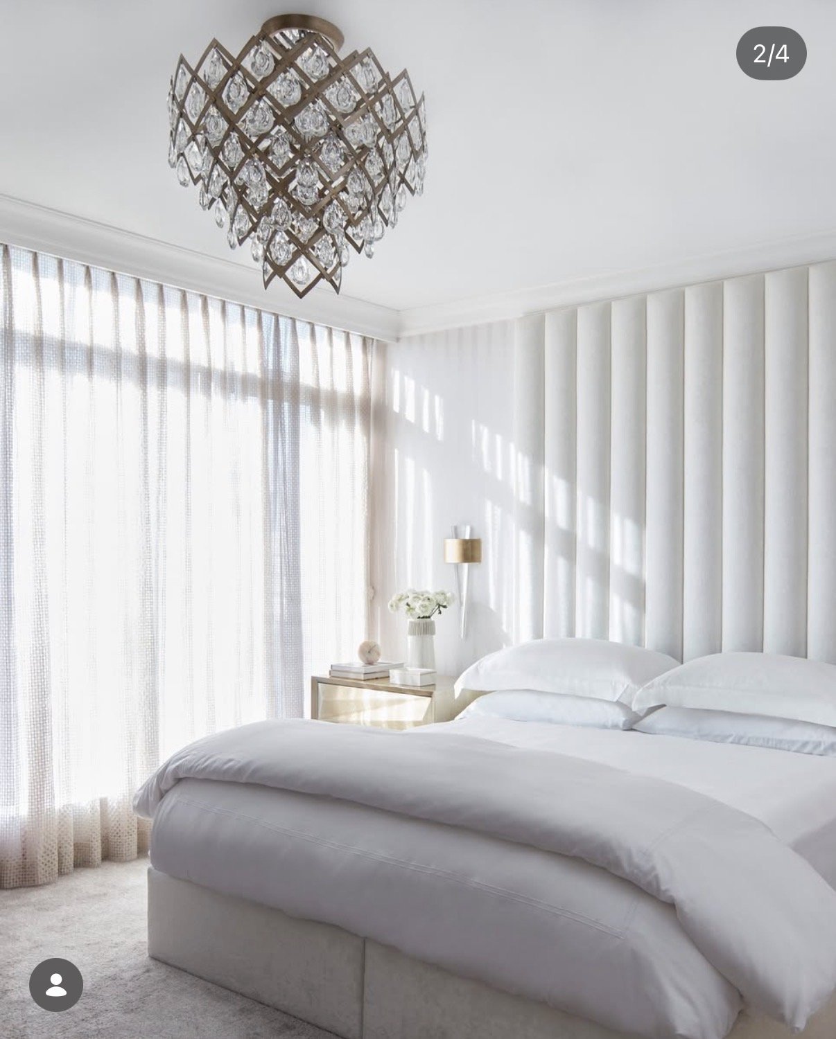All-white bedroom with vertical channel headboard, sheer linen drapery and crystal chandelier NYC