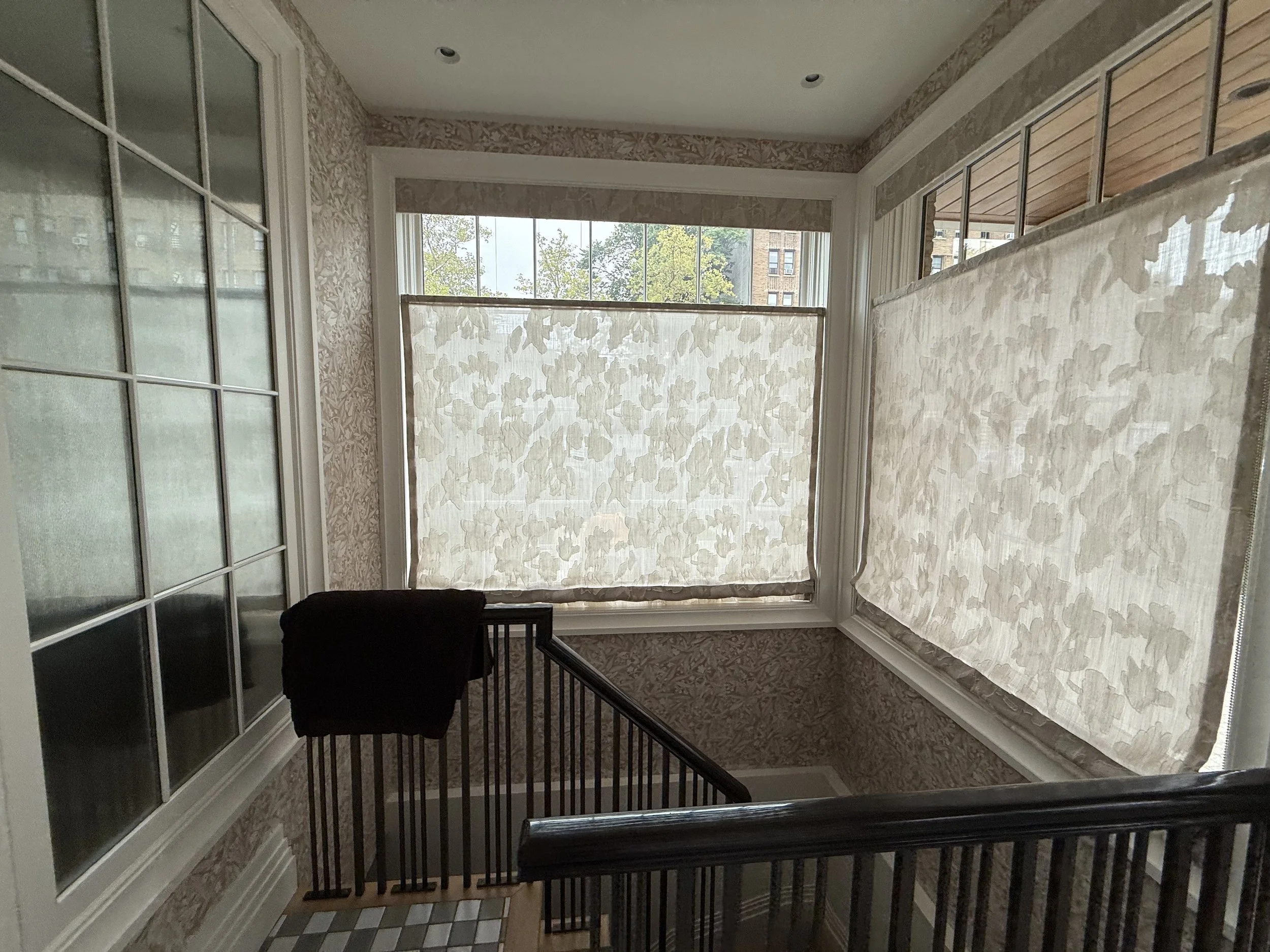 Botanical patterned roman shades on multiple staircase landing windows with matching wallpaper, NYC custom shades