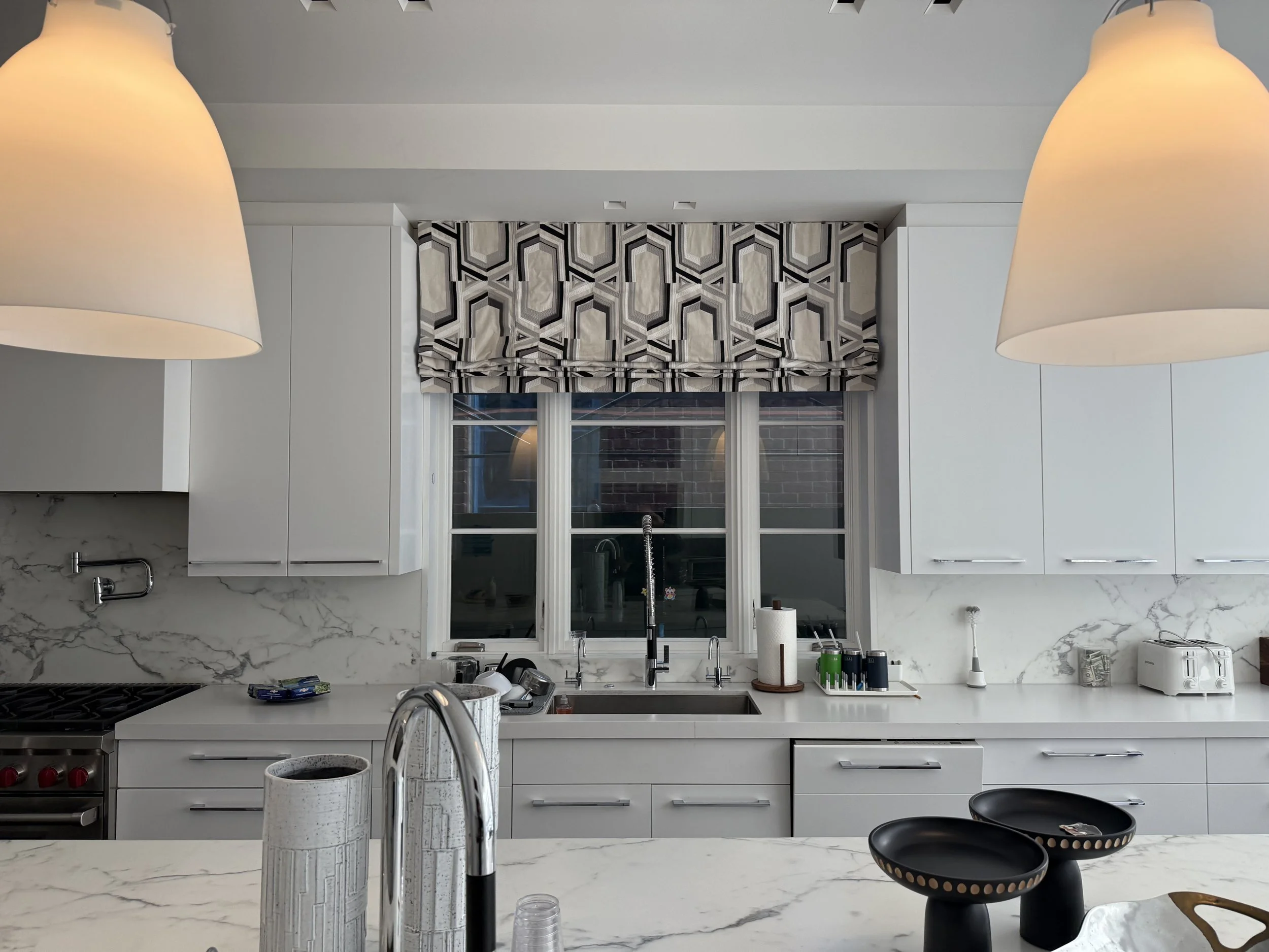 Bold geometric patterned roman shade in modern white kitchen with marble backsplash and bar stools, NYC