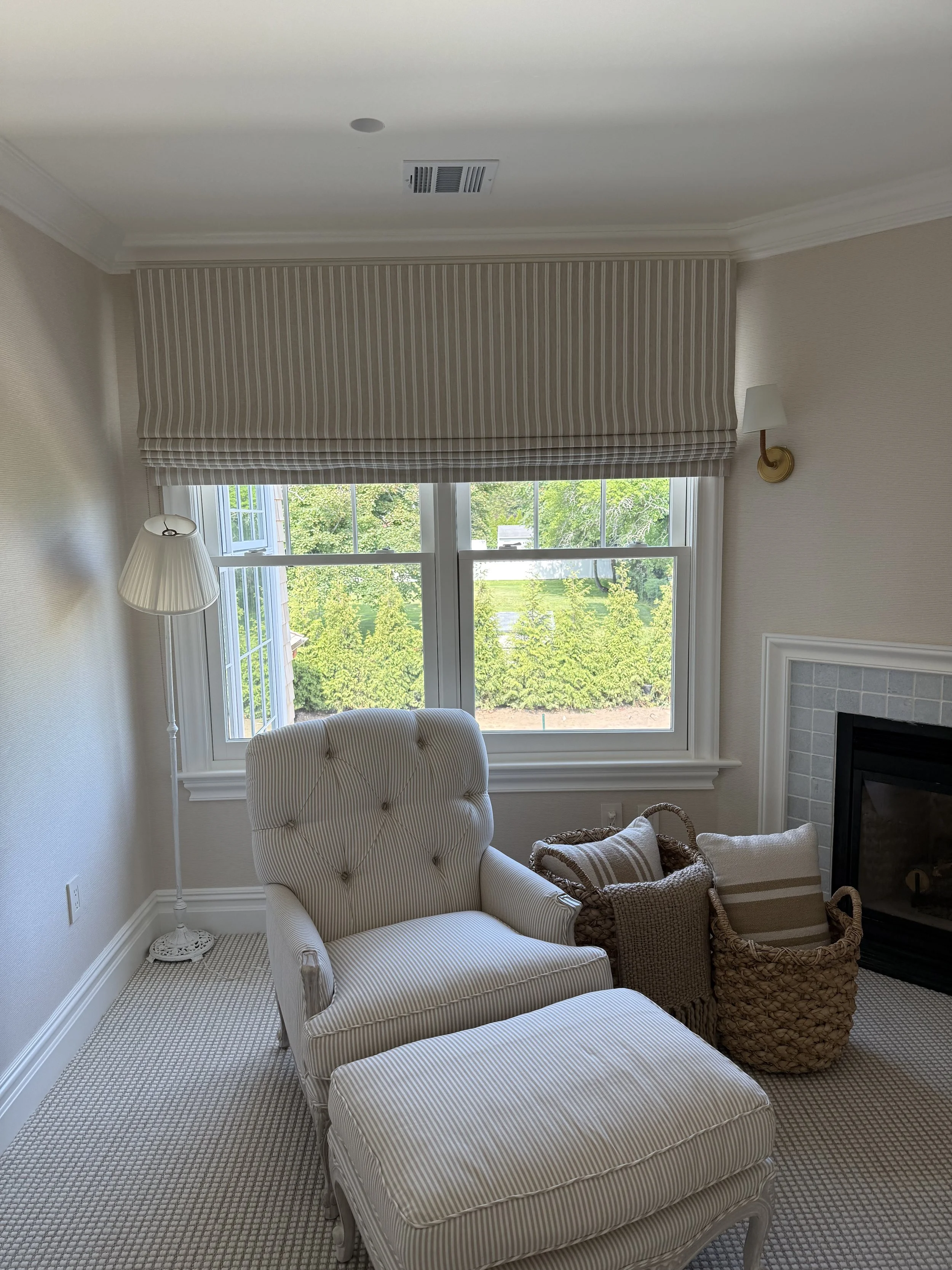 Ticking stripe relaxed roman shade above garden window in cozy reading nook with tufted armchair and fireplace, NYC