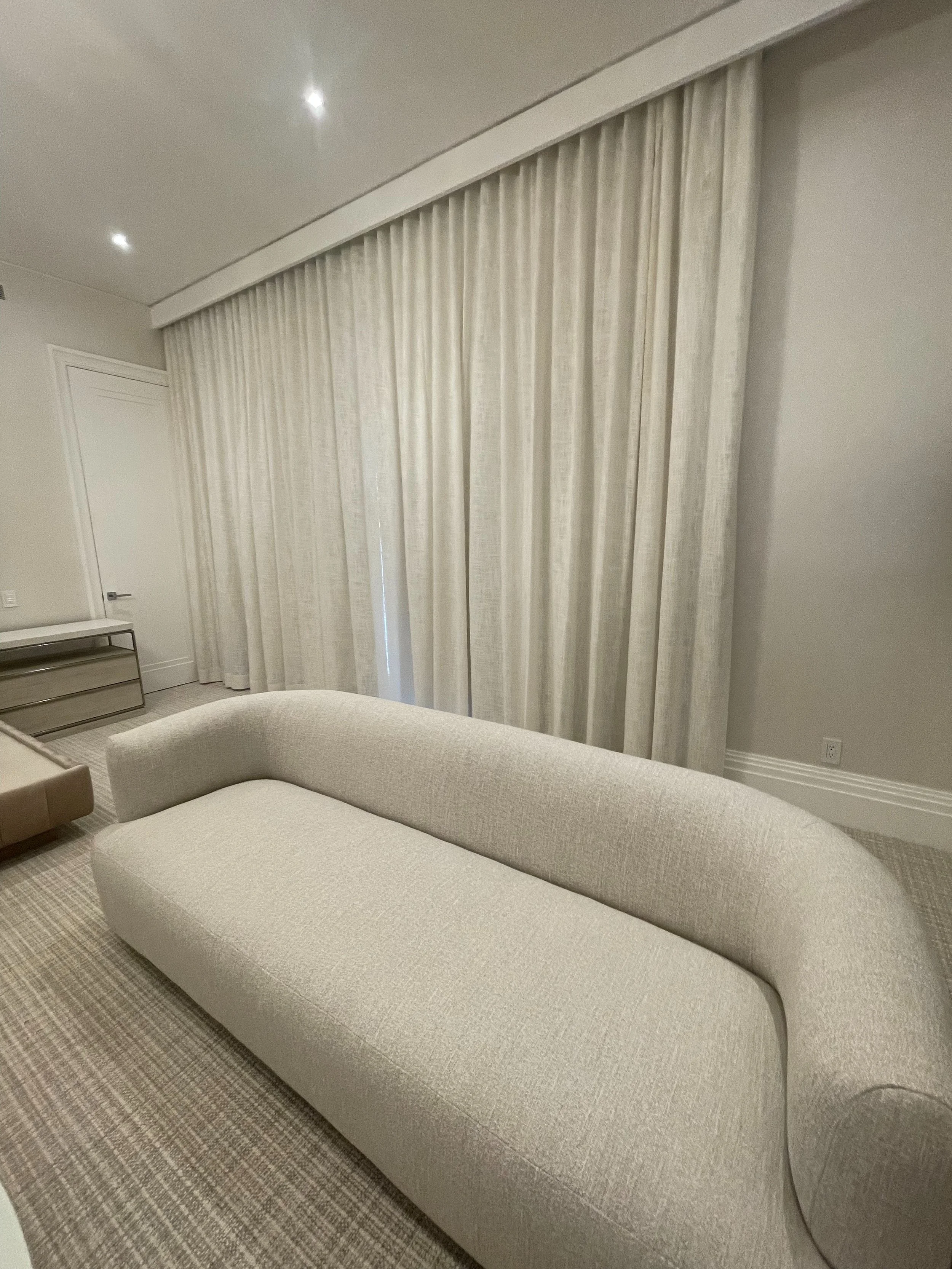 Custom plantation shutters in elegant breakfast room with arched bay windows, glass dining table and crystal chandelier, NYC