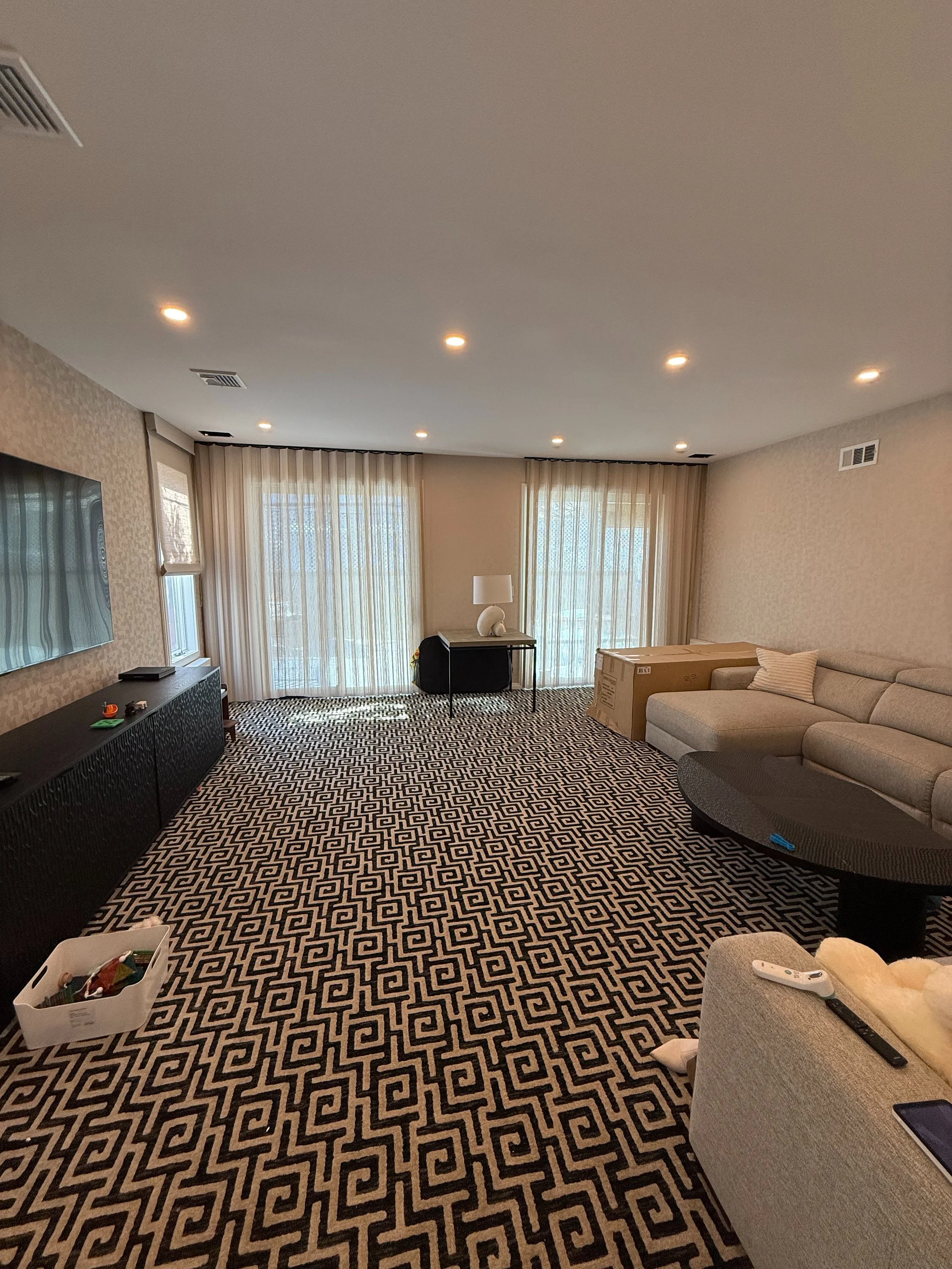 Modern living room with floor-to-ceiling sheer ripple-fold drapery on ceiling track and bold geometric rug NYC