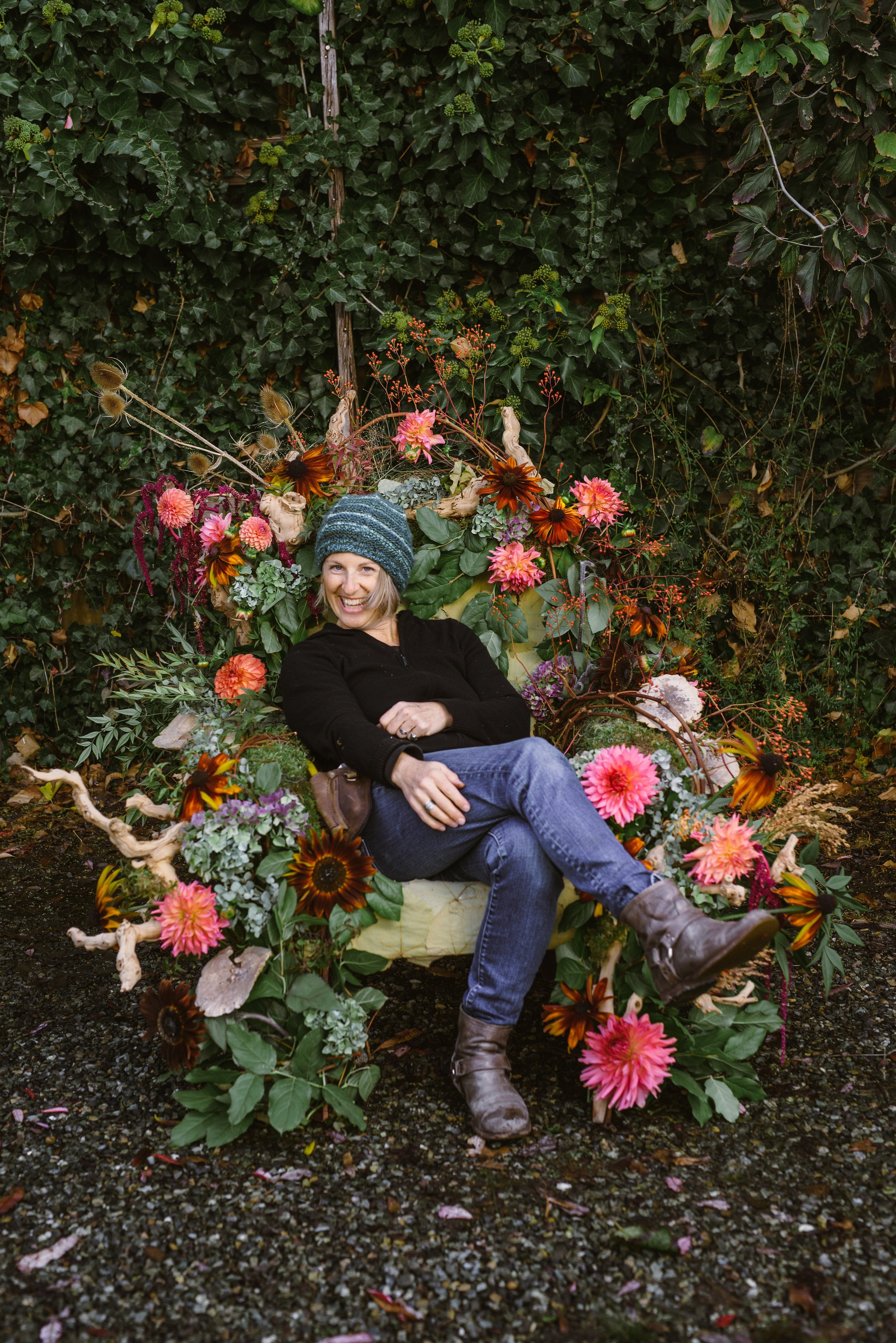 Tobey Nelson is a horticulturist on Whidbey Island. She is sitting in a chair made from flowers and branches.