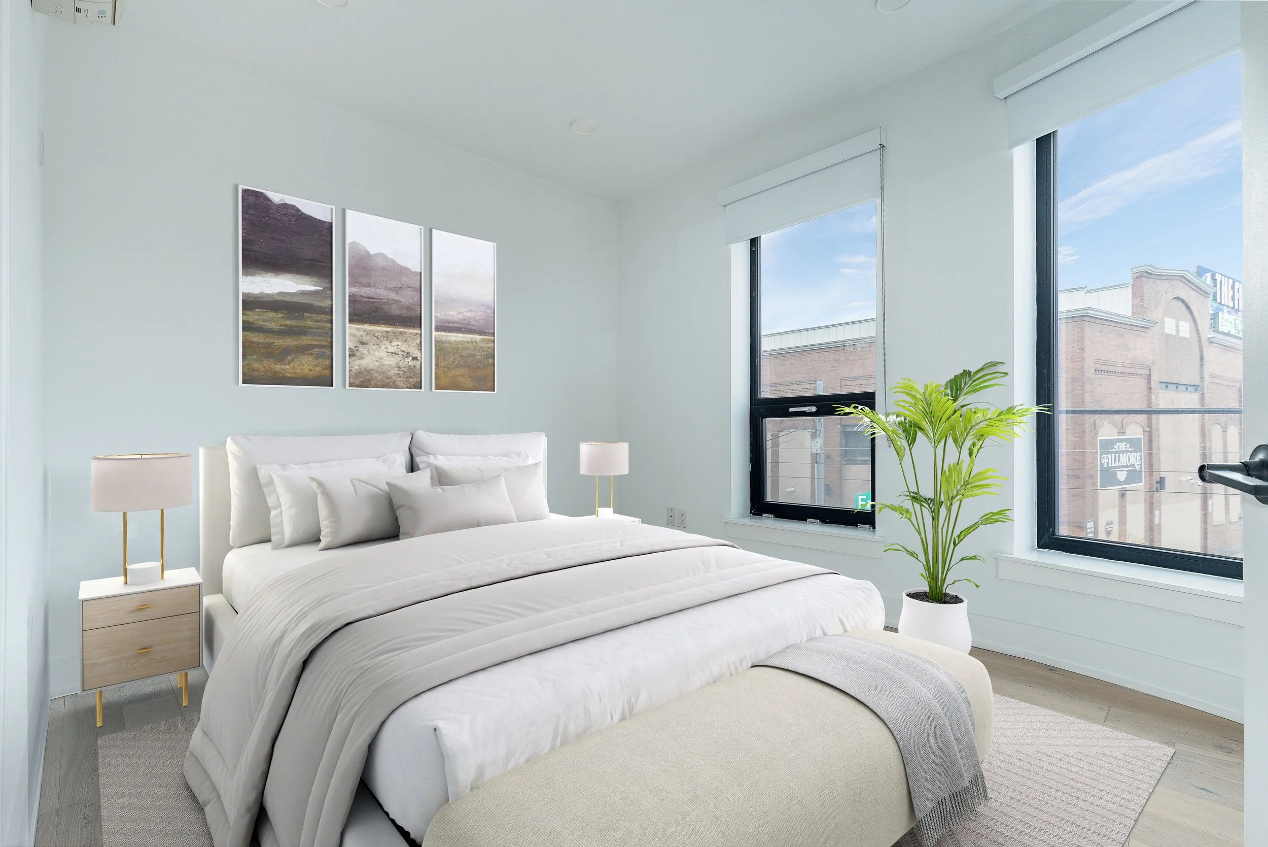 Bright bedroom with white bedding, two nightstands with lamps, large windows, green plant, and abstract landscape wall art.