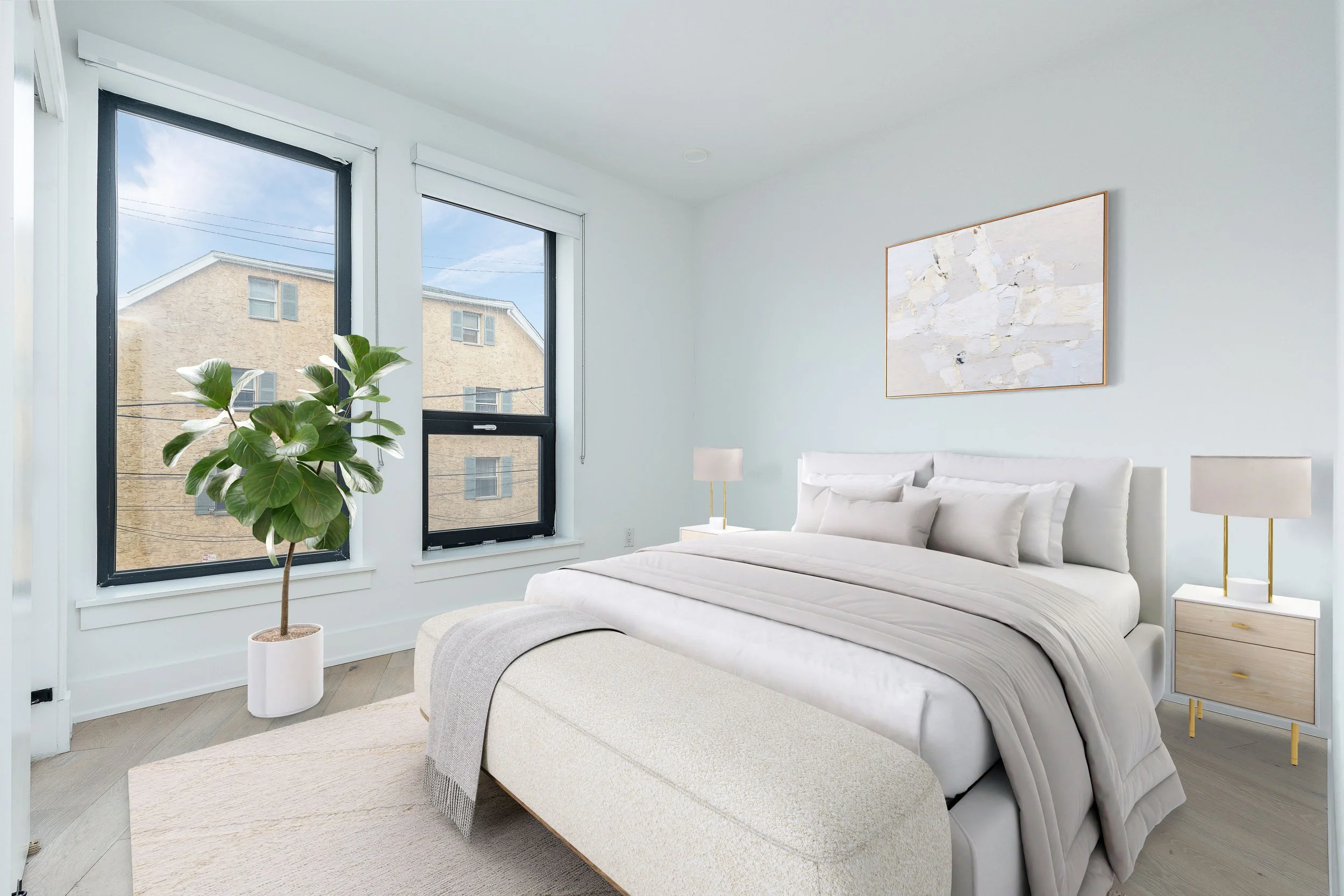 Bright minimalist bedroom with white walls, large windows, a white bed with pillows, two bedside tables with lamps, a beige ottoman at the foot of the bed, a large green potted plant, and a modern abstract painting on the wall.
