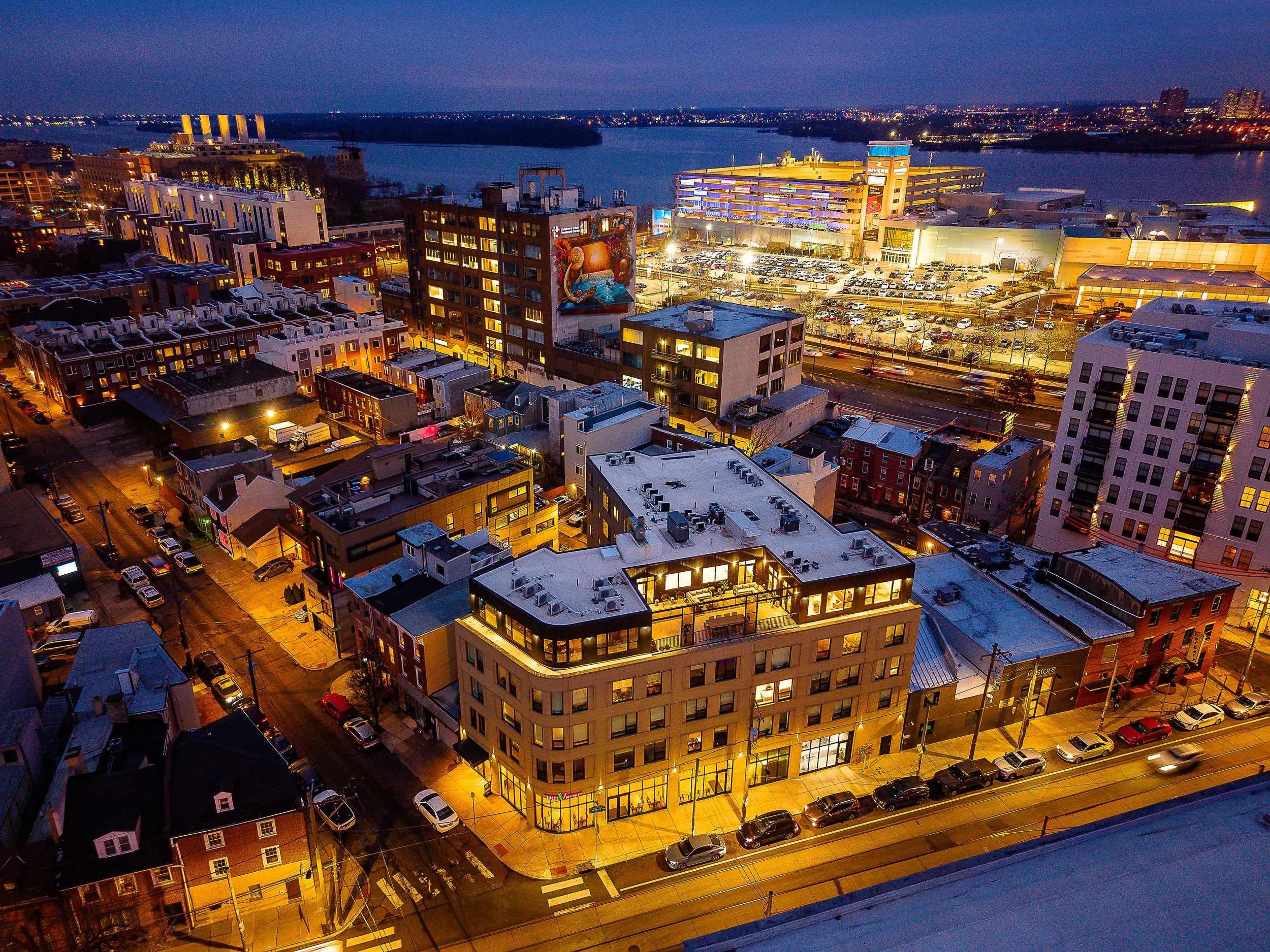 A cityscape at dusk with illuminated buildings, streets, and a river in the background.