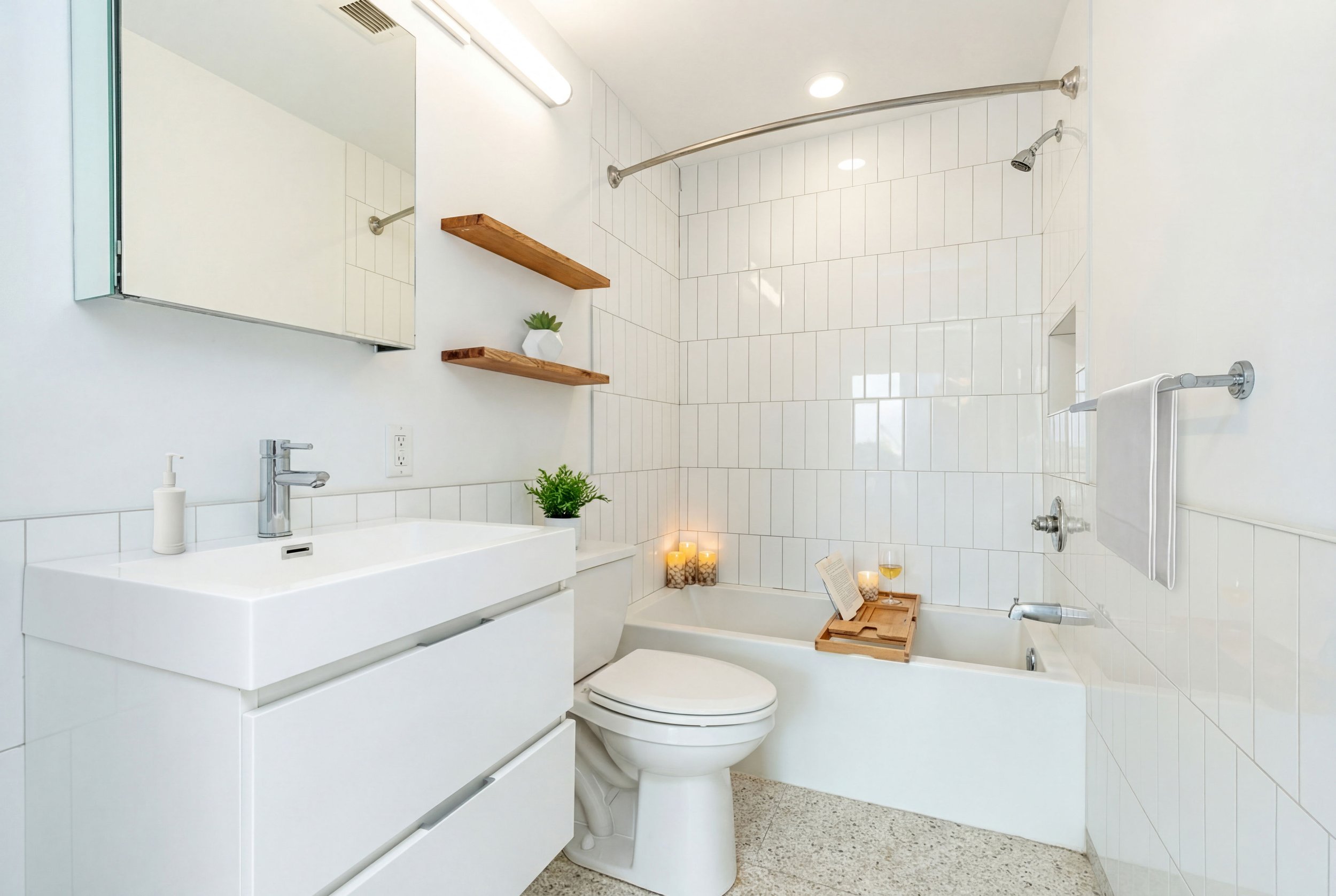 Modern white bathroom with a rectangular sink, a mirror cabinet, wooden shelves, a potted plant, candles, a bathtub with a tray, and a towel bar.