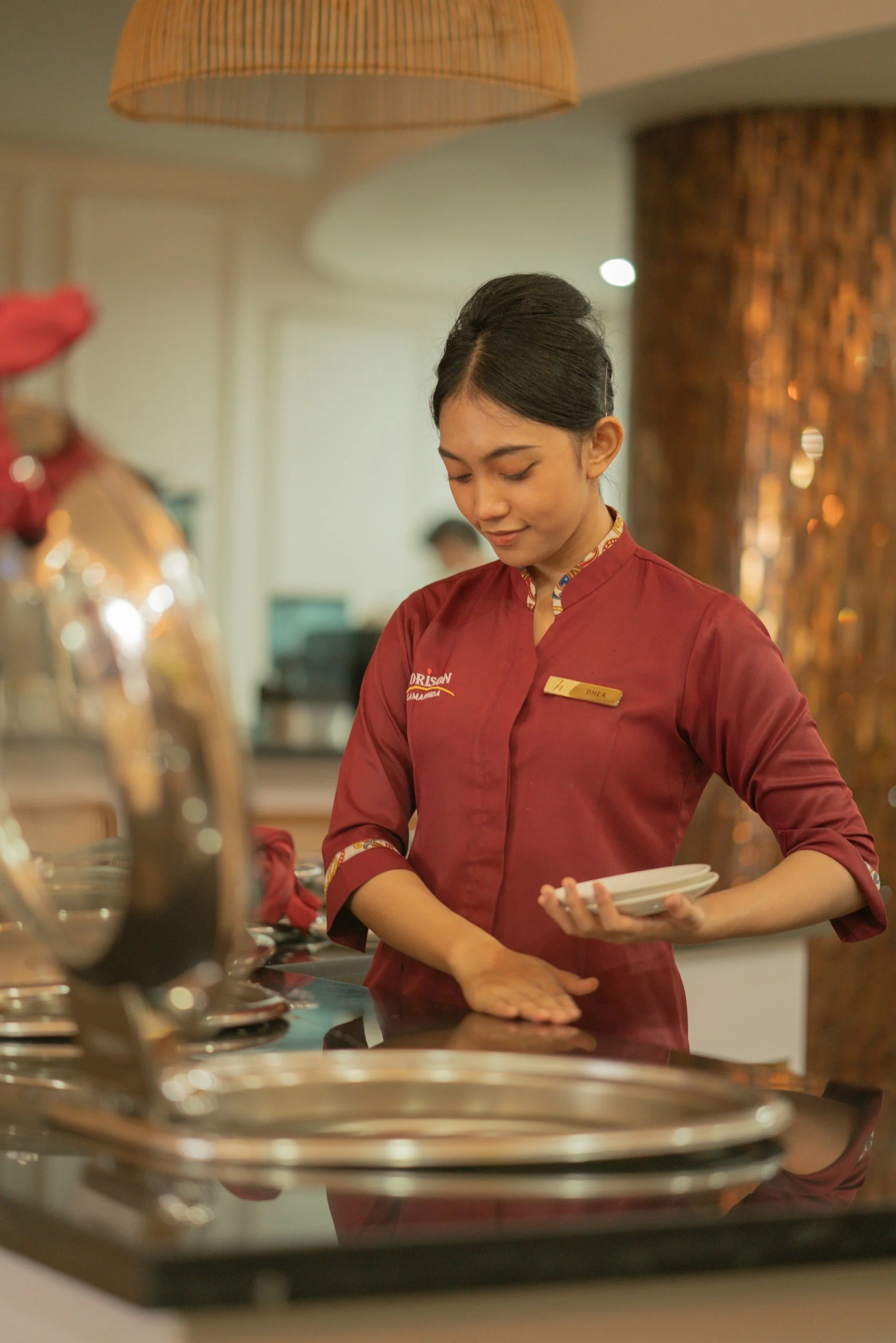 Una mujer con uniforme de trabajo en un establecimiento de comida, sosteniendo un plato, en un entorno de restaurante.