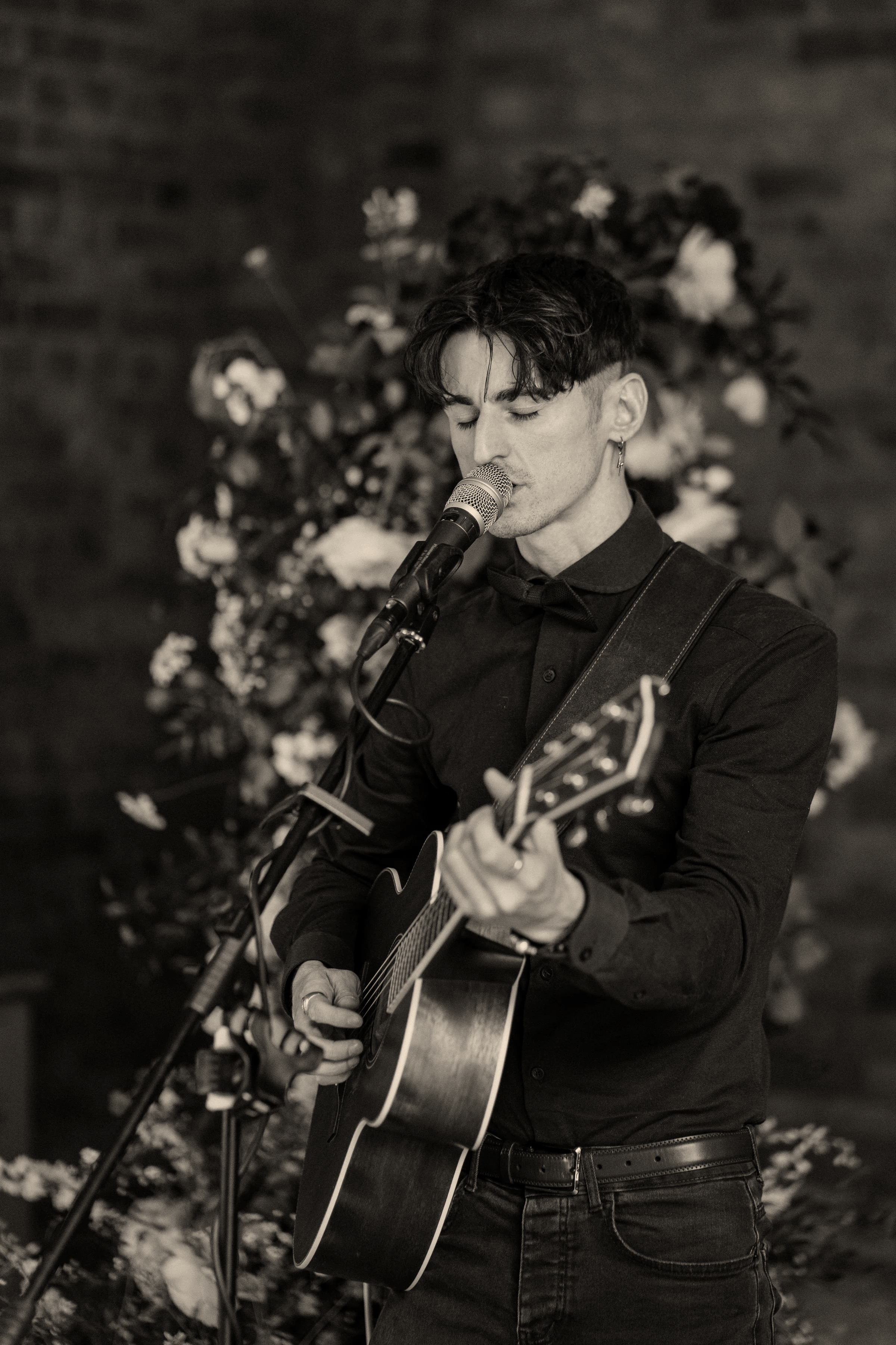 A young man singing and playing an acoustic guitar with a floral wedding background.