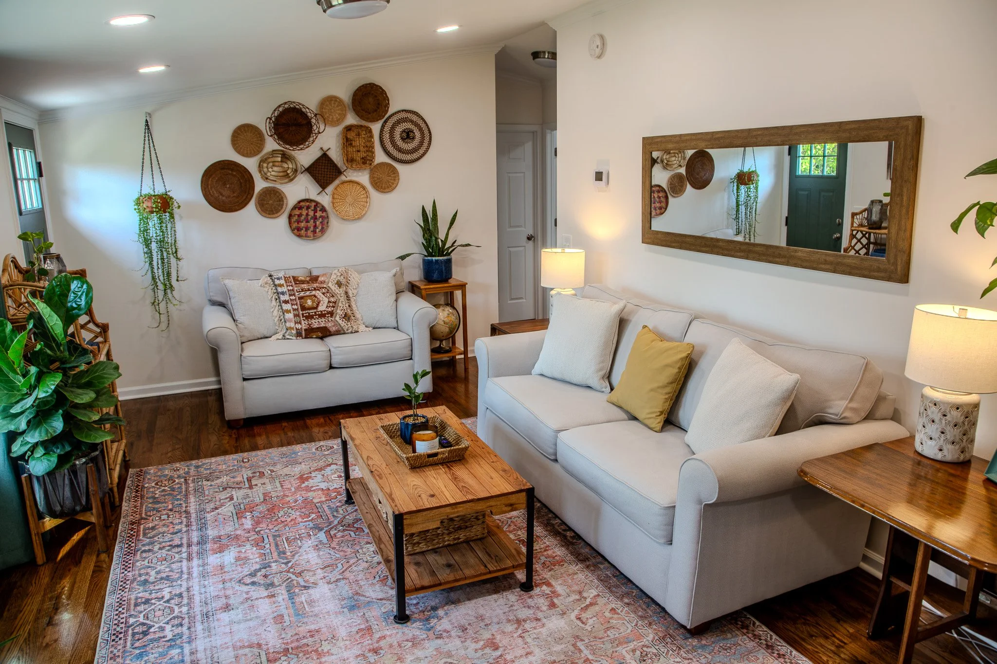 Living room with two white sofas, wooden coffee table, a large mirror, and wall decor of woven baskets.