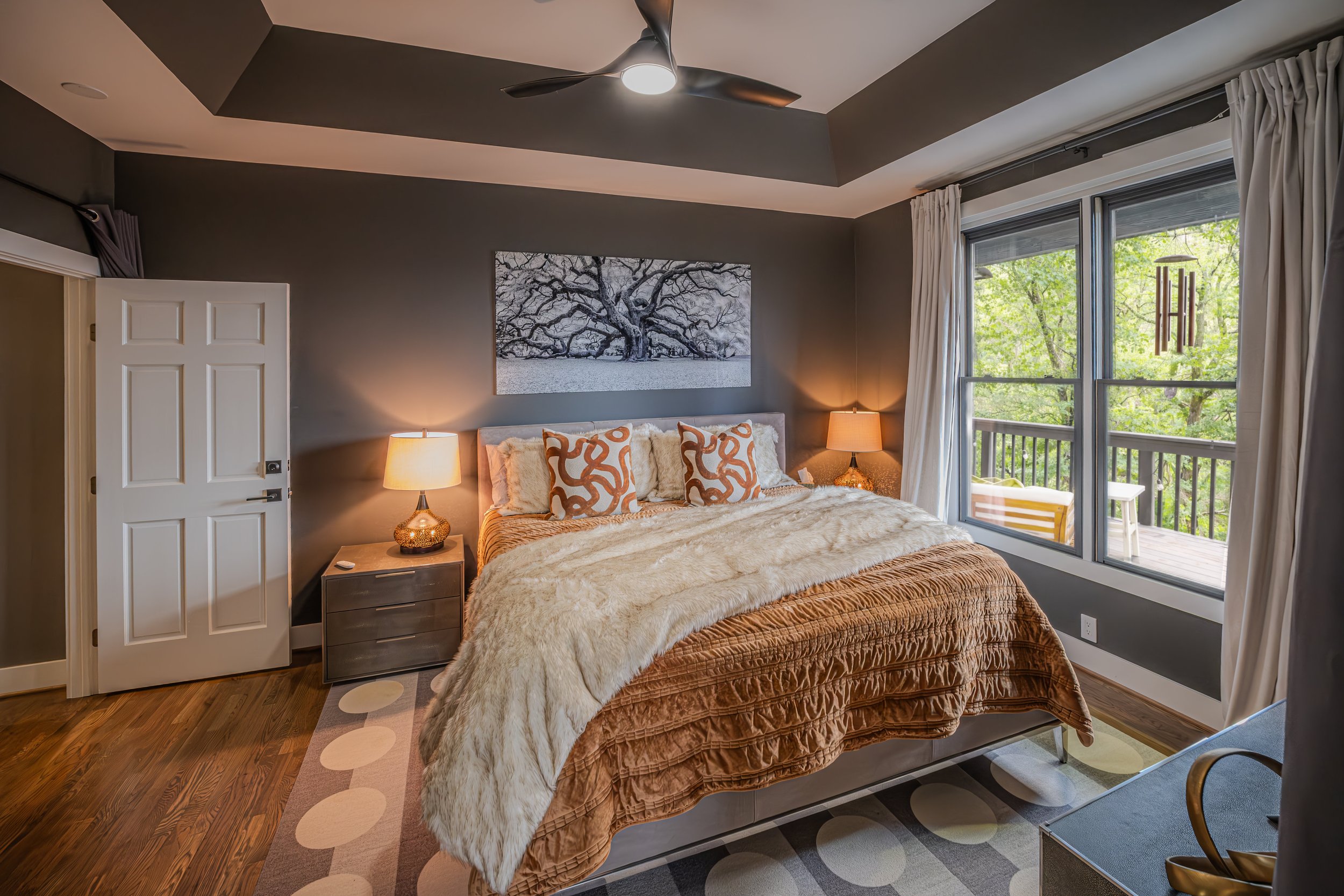 Side view of a blue house with stone stairs and a white door, surrounded by green trees and a lawn with small plants.