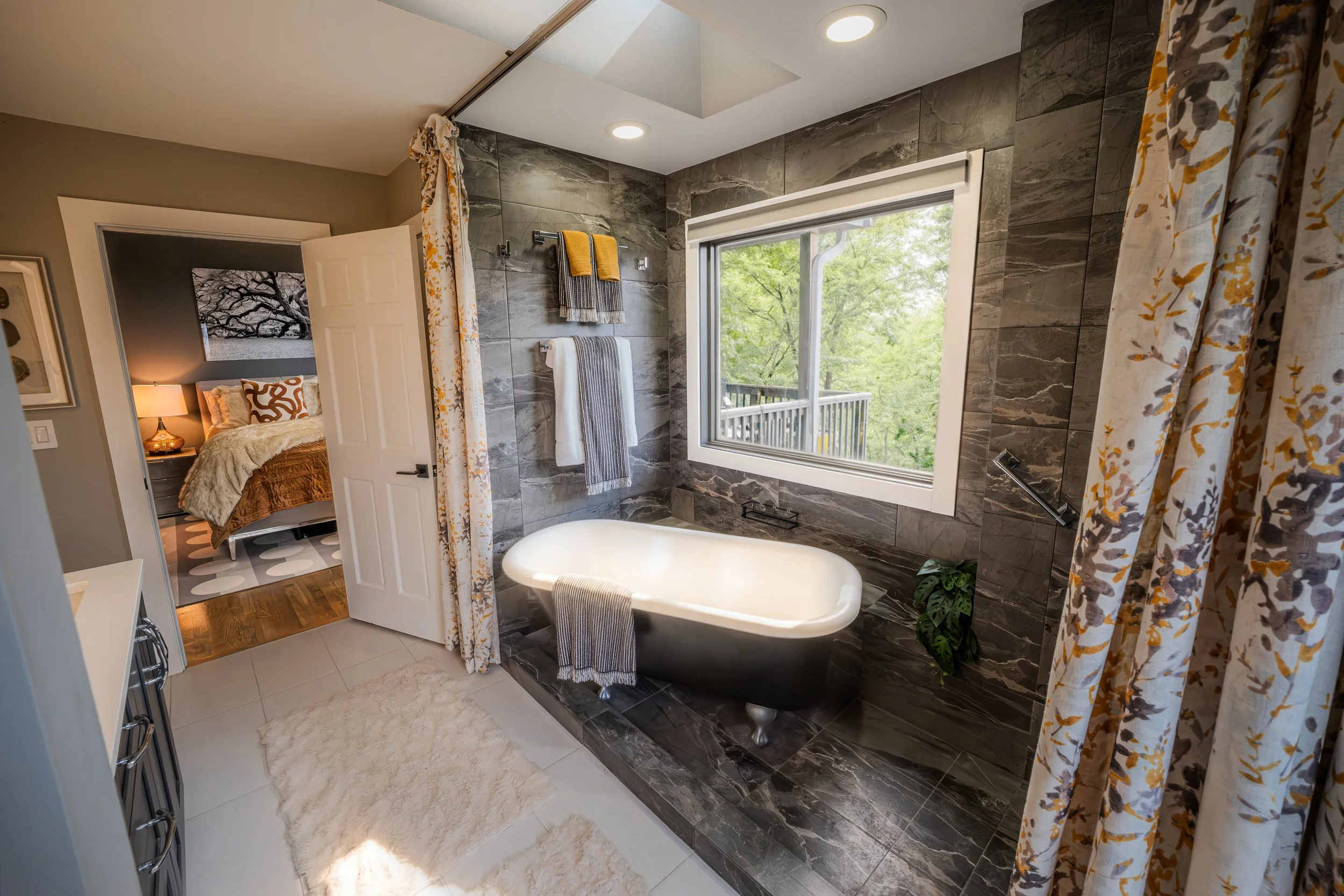 Cozy living room with white sofa, wooden coffee table, patterned area rug, and plant decor, connected to kitchen with stainless steel refrigerator.