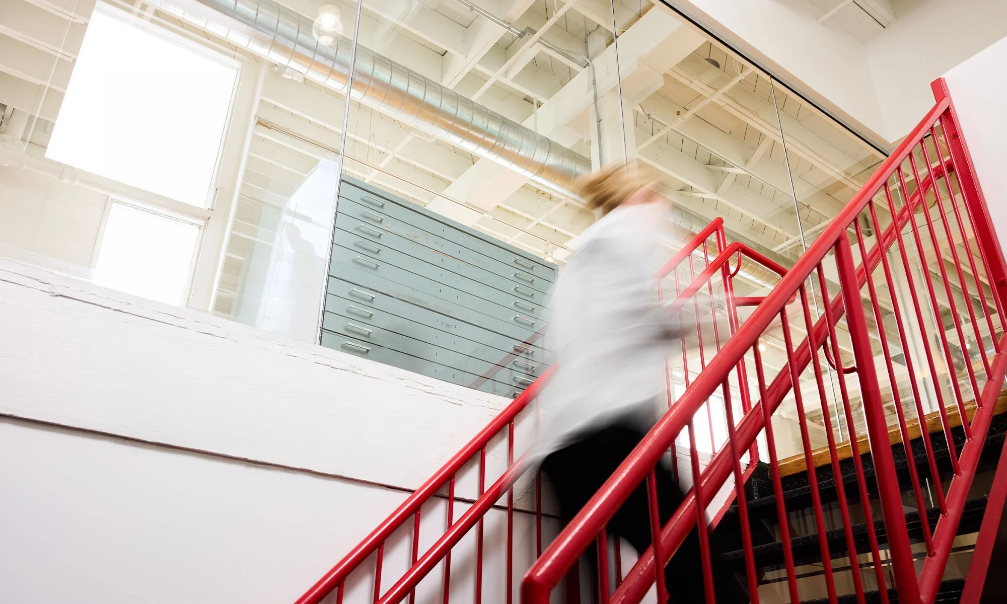 A person in motion, blurred, walking up a black staircase with vibrant red railings.