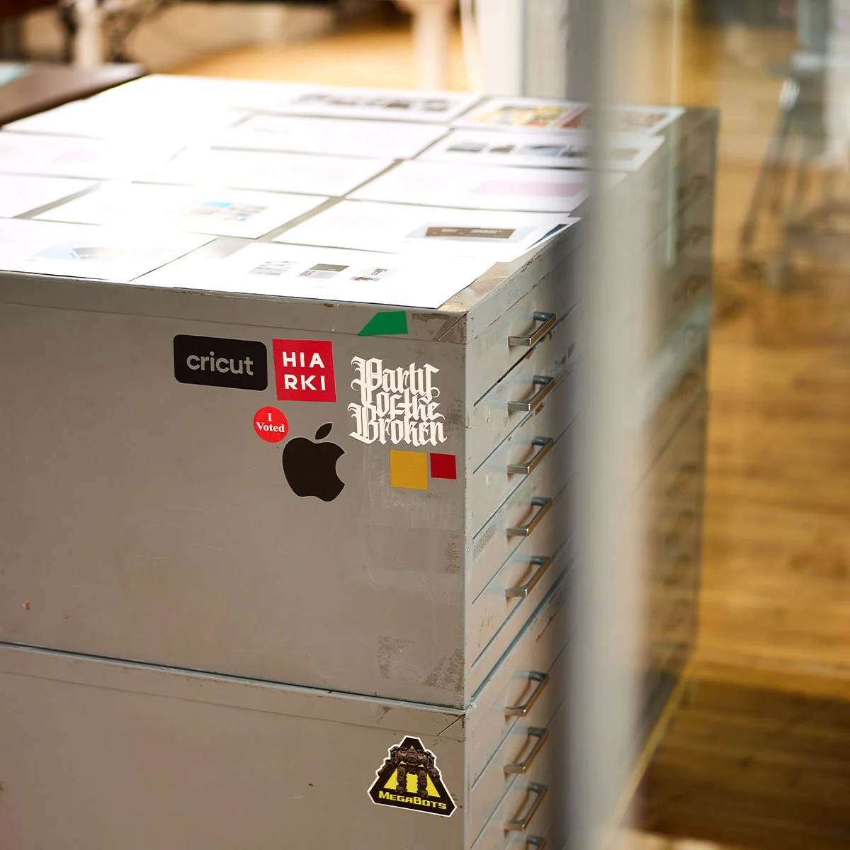 A stack of grey metal flat-file cabinets with design proofs spread across the top surface.