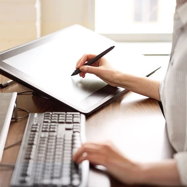 A close-up, shallow-focus shot of a person's hand using a digital stylus pen on a tilted drawing tablet.