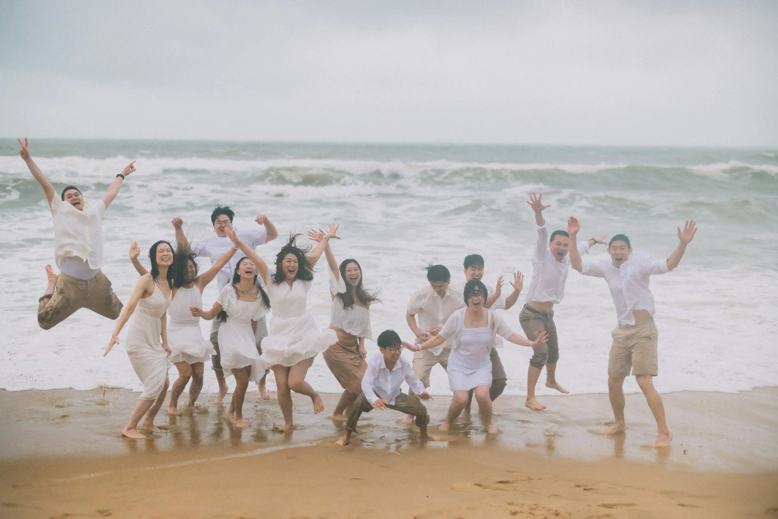 A group of people is playing and jumping at the beach near the ocean waves, all smiling and enjoying themselves.