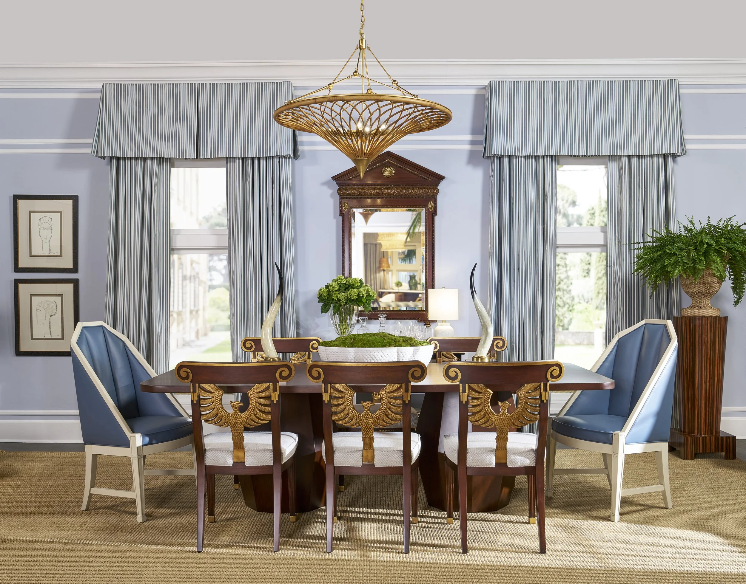 A dining room with a wooden table, six blue and white chairs, a large mirror, and a chandelier hanging from the ceiling, with two windows and striped curtains.
