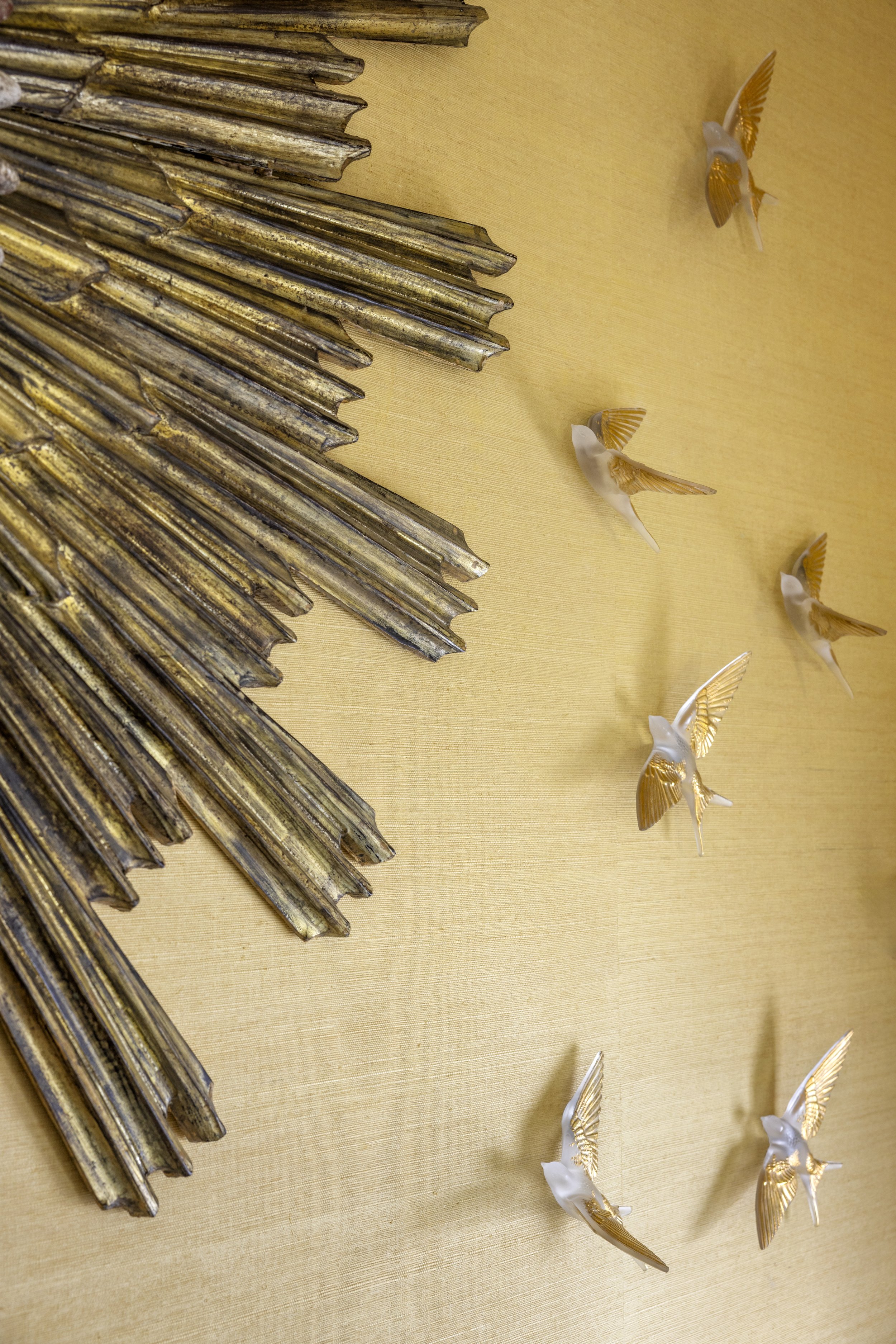 Decorative art piece with elongated, weathered metallic elements on a beige background, and several small angel figurines with gold wings.