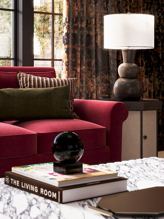 Interior living room scene with a red sofa, decorative pillows, a side table with a lamp, a window with dark floral curtains, and a marble coffee table with books and a black sphere sculpture.