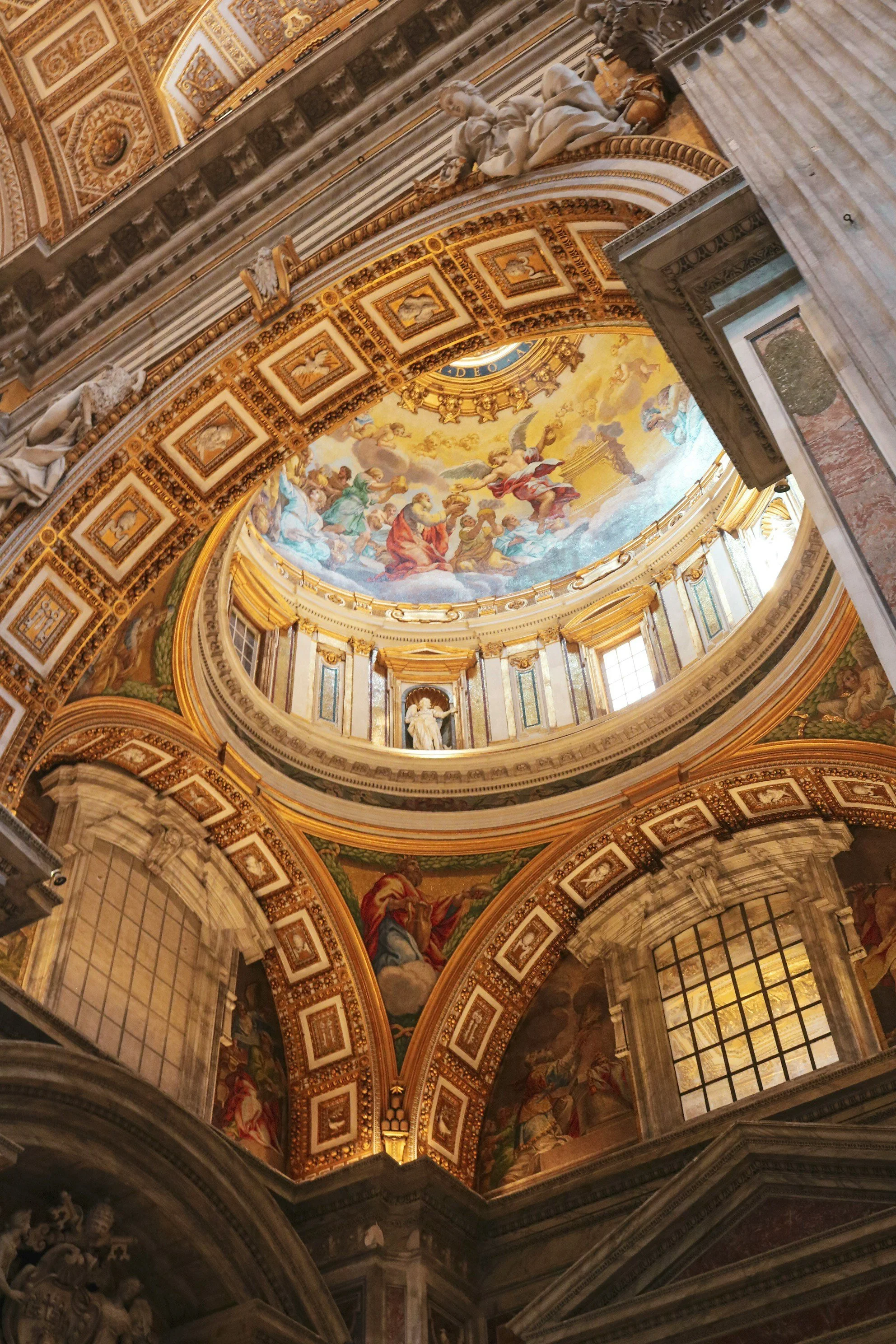 Interior view of a grand church ceiling with elaborate gold and colorful frescoes, sculptures, and architectural details.