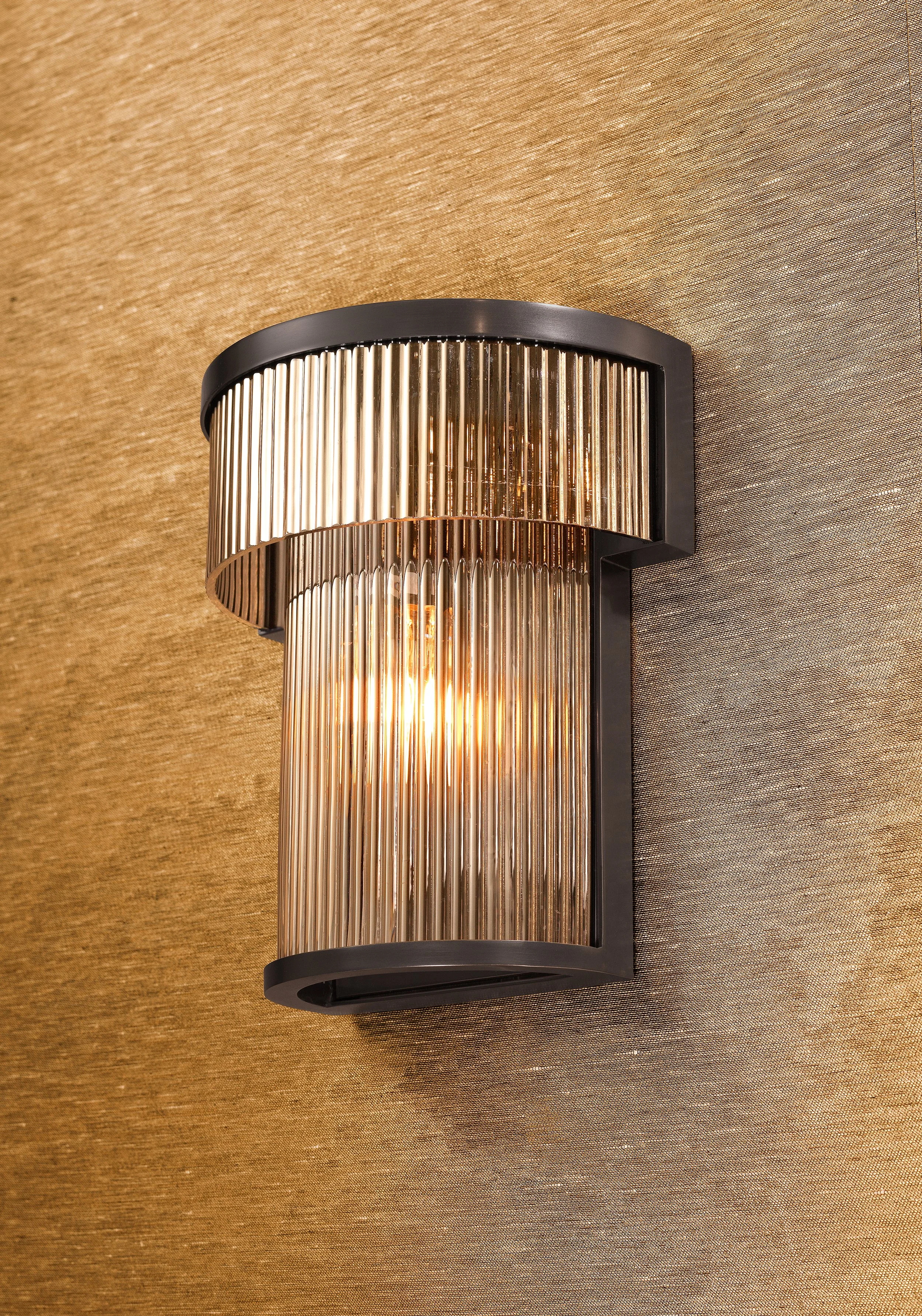 Modern wall sconce with a black frame and vertical glass rods mounted on a textured brown wall.