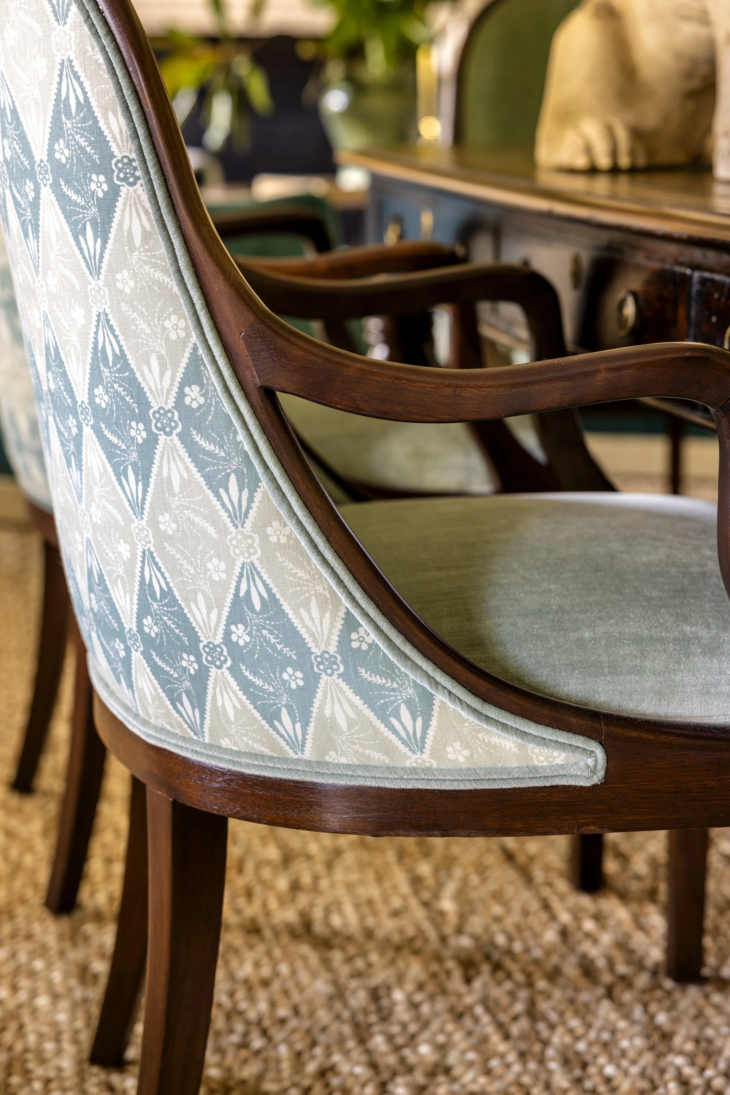 Close-up of vintage wooden chairs with upholstered seats and backs, textured fabric with light blue and white pattern, set on a speckled brown carpet.