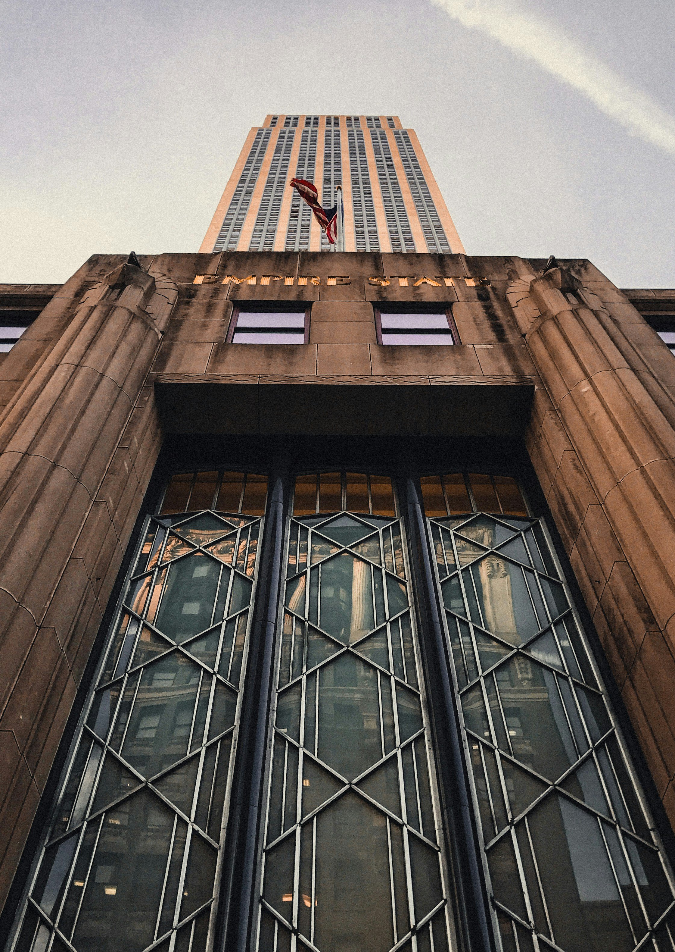 Looking up at a tall skyscraper with an American flag and a city flag flying from the top, and the building's name ‘HUMPHREY SULTAN’ engraved on the front facade near the entrance.