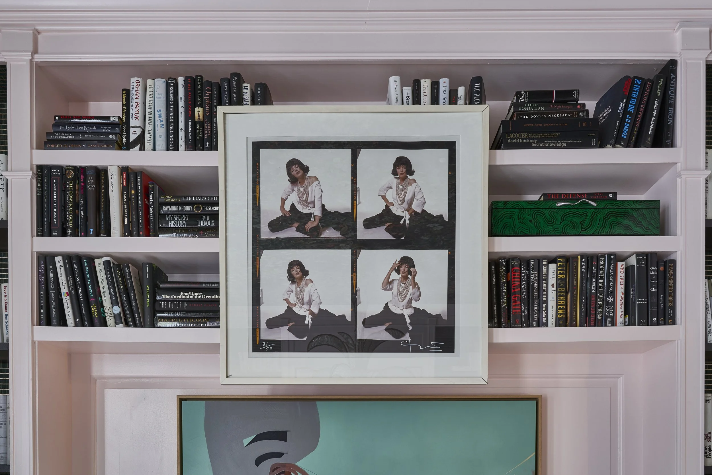 Bookshelf filled with numerous books, with a framed photo of a woman in different poses in front of the shelf. Part of a large, colorful abstract art piece is visible at the bottom of the image.