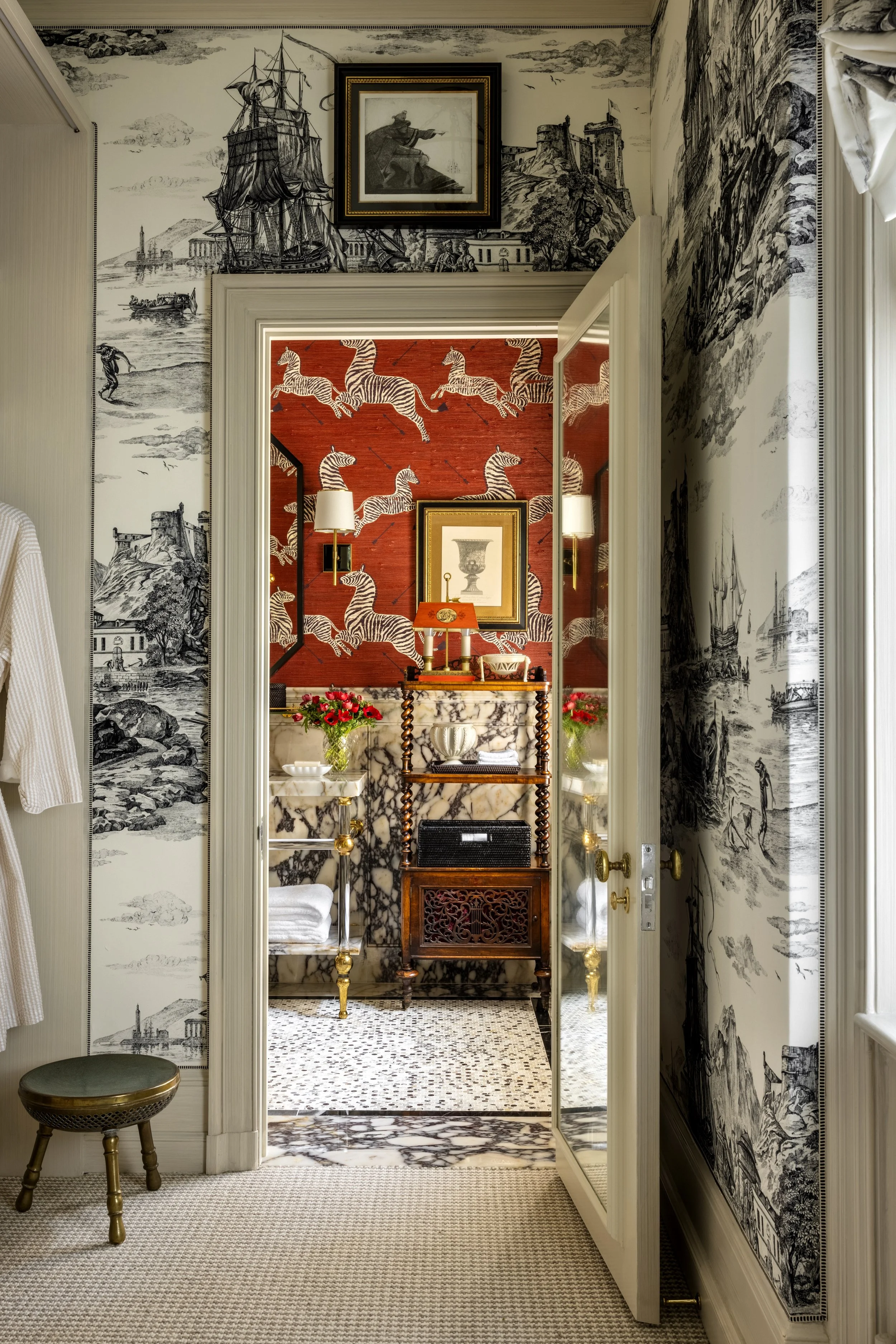 Interior view of a luxurious hallway with black and white vintage illustrations on the walls, ornate furniture, and a red wallpapered room featuring zebra patterns visible through a doorway.