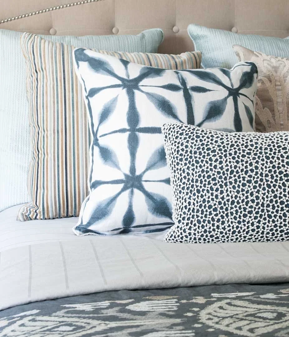 Multiple decorative pillows with various patterns and colors arranged on a bed with a light-colored headboard.