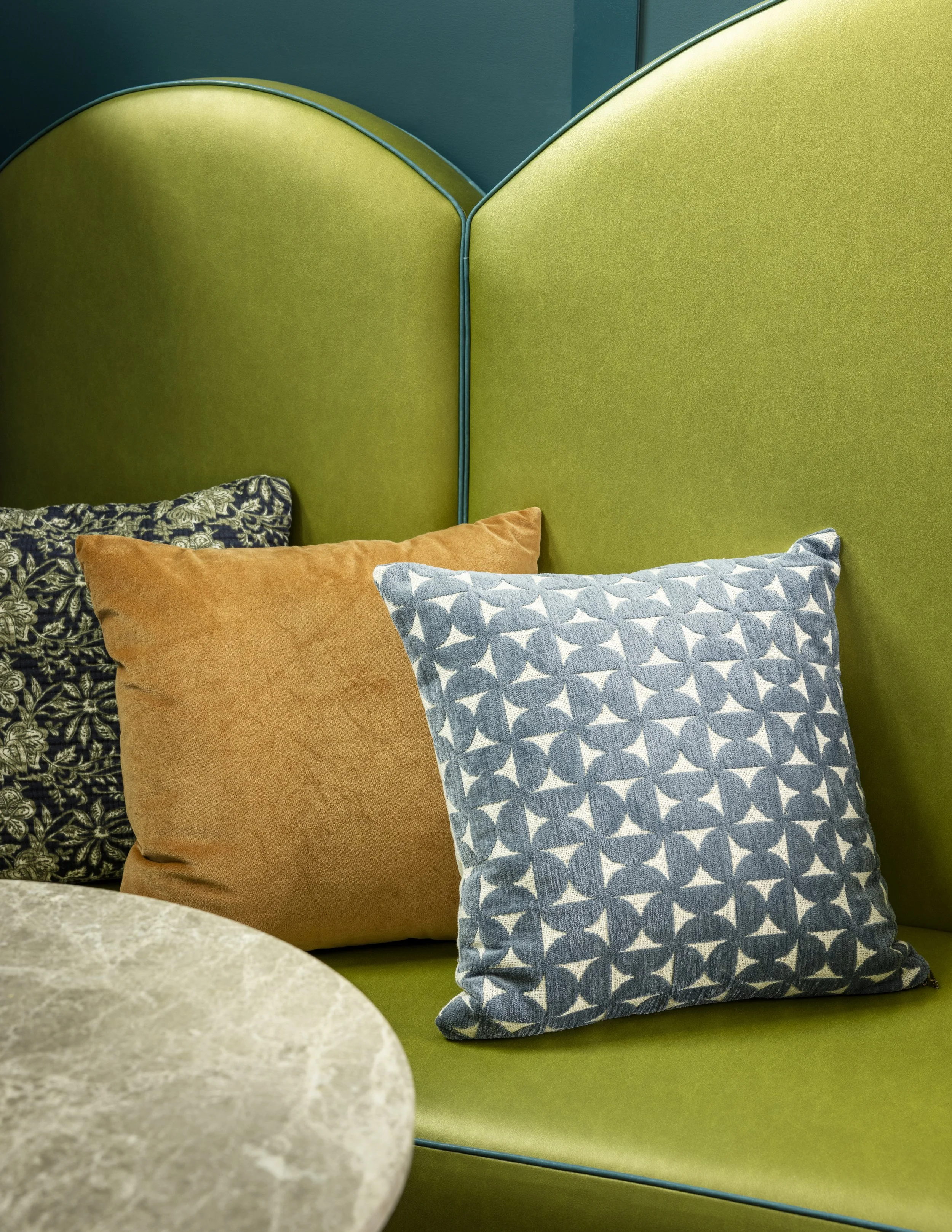 Close-up of a green upholstered booth with decorative pillows in front of a table.
